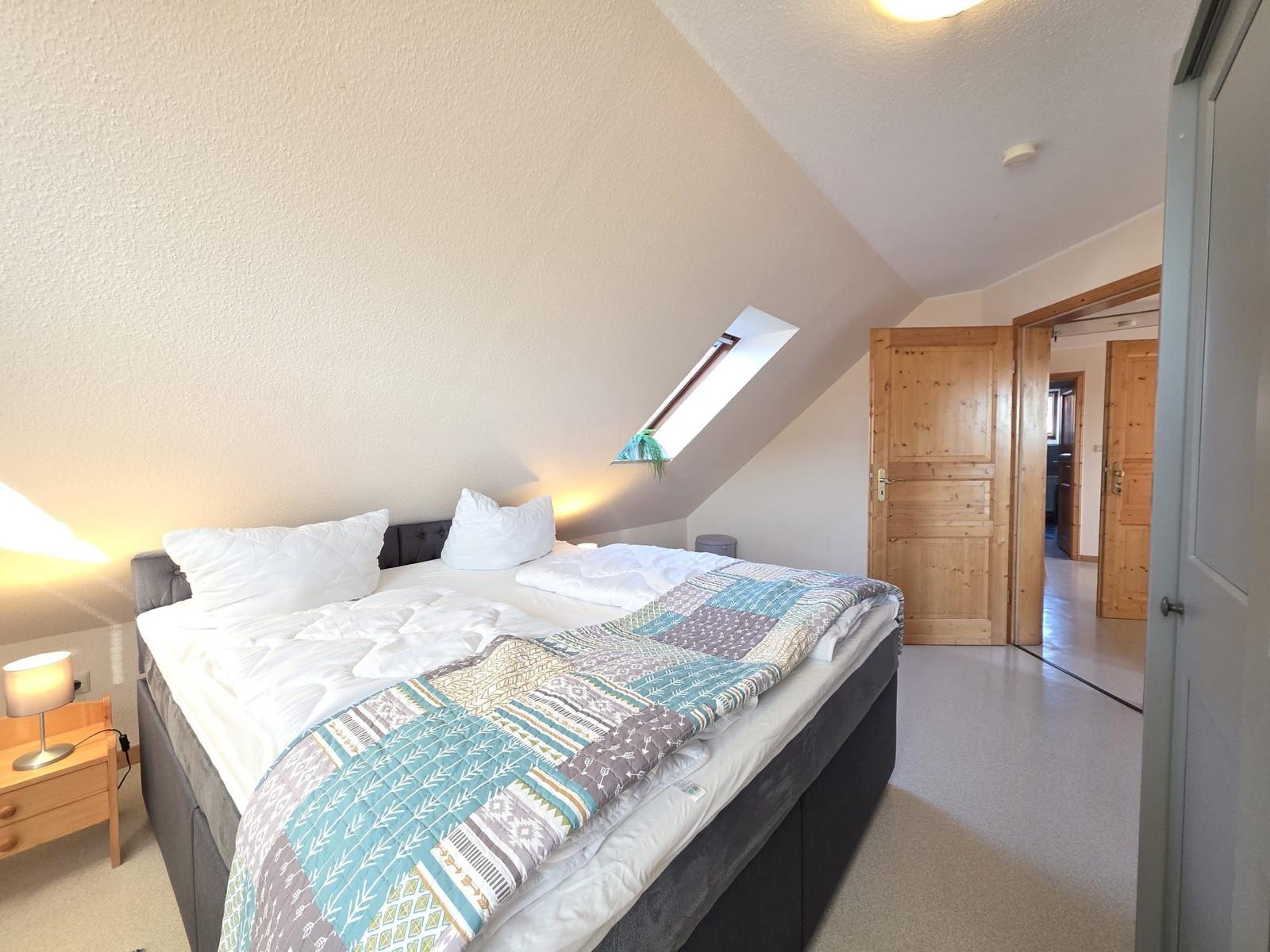 Schlafzimmer mit Dachschrägen, Bett, Nachttisch und Dachfenster.
