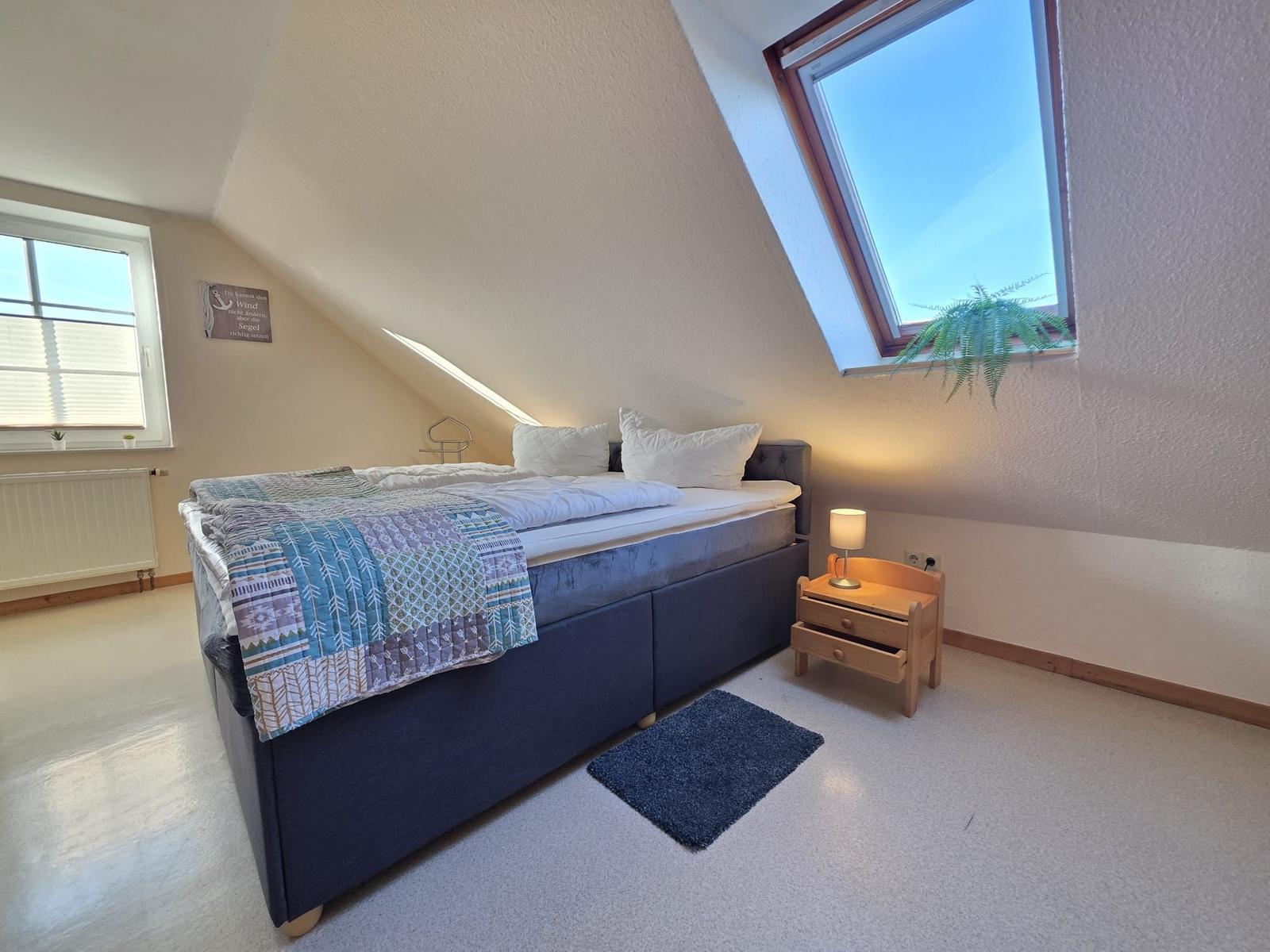 Schlafzimmer mit Dachschrägen, Bett, Nachttisch und Fenster.