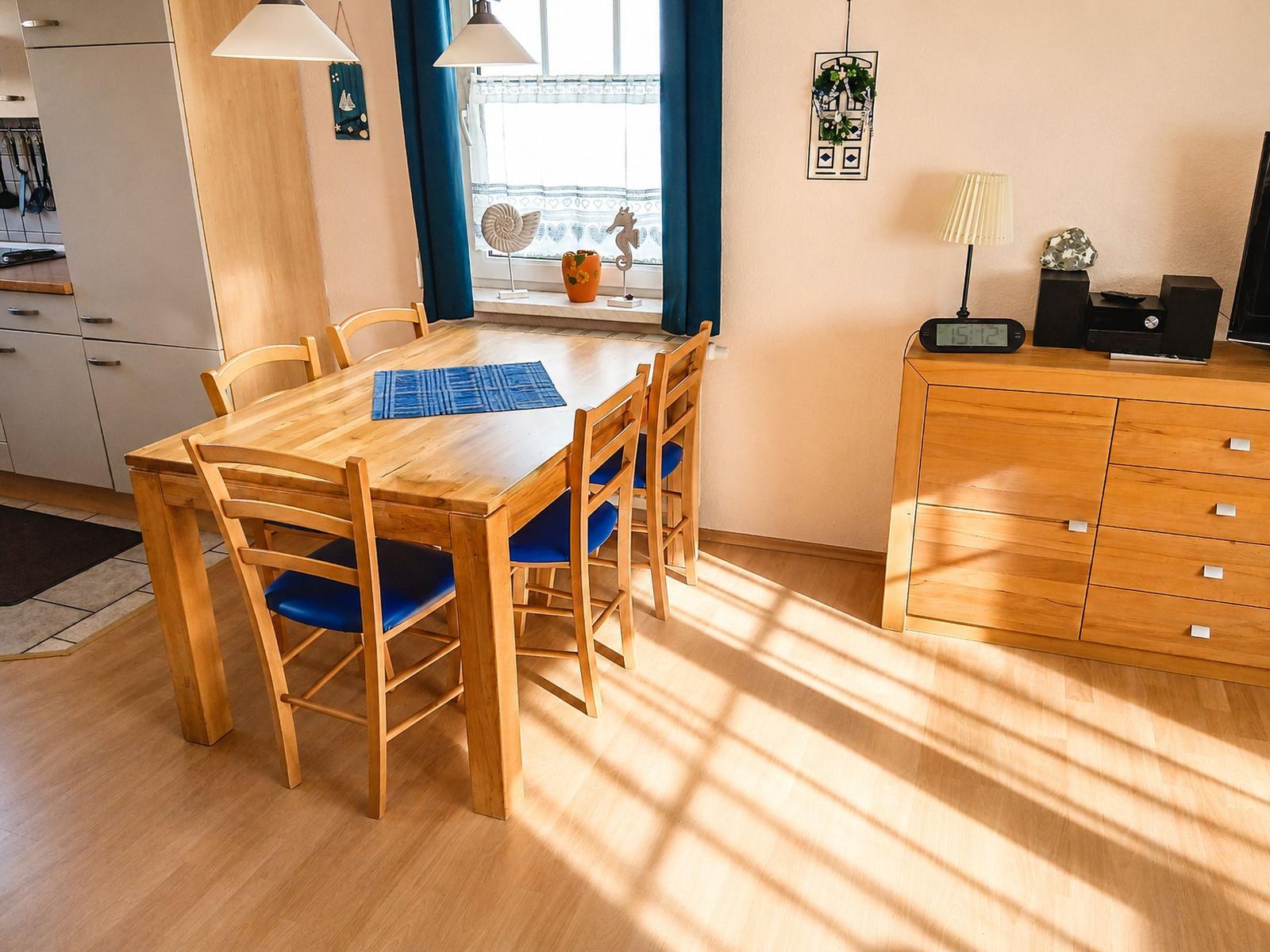 Essbereich mit Holztisch, vier Stühlen und Fenster mit Vorhängen.