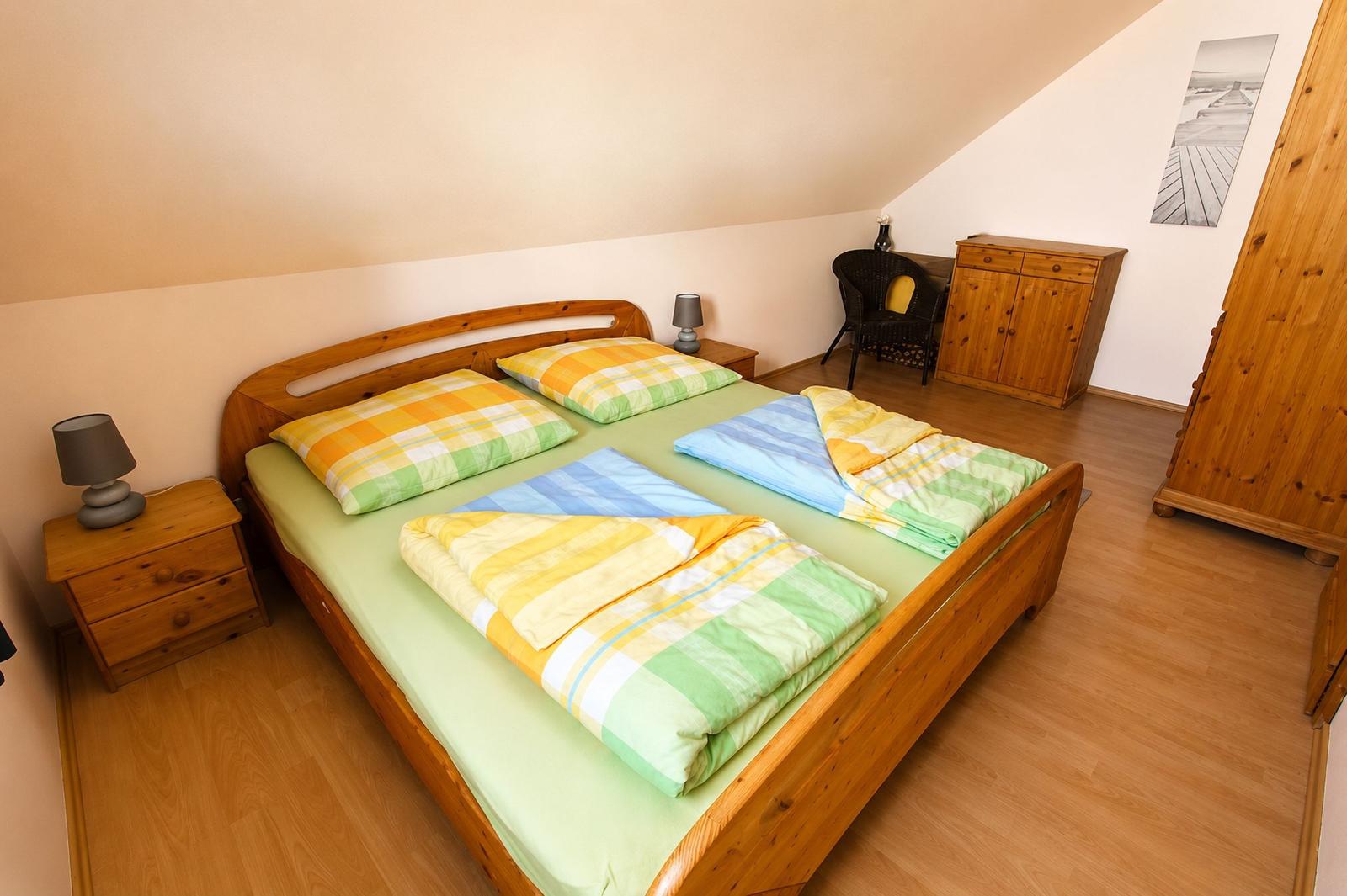 Schlafzimmer mit Doppelbett, Holzmöbel und Holzboden. An der Wand hängt ein Bild.