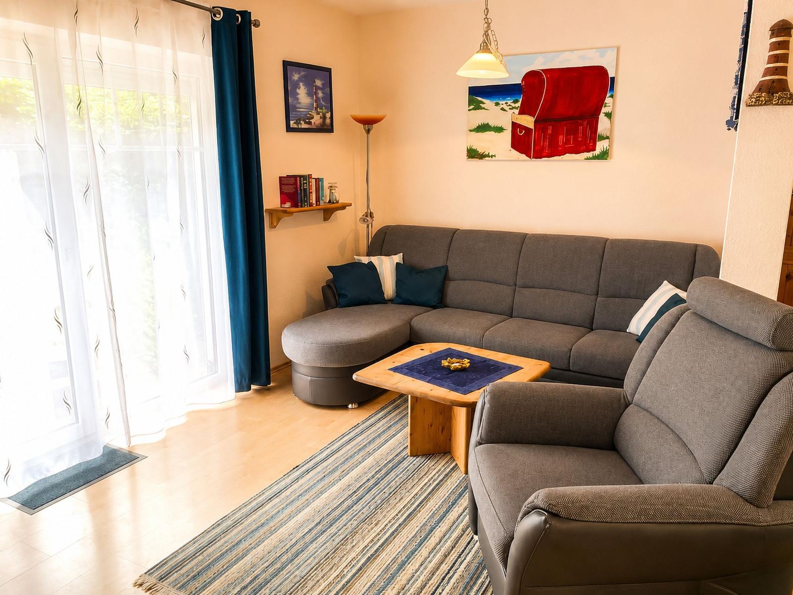 Wohnzimmer mit grauem Sofa, Holztisch und blauem Teppich. Fenster mit weißen und blauen Vorhängen.