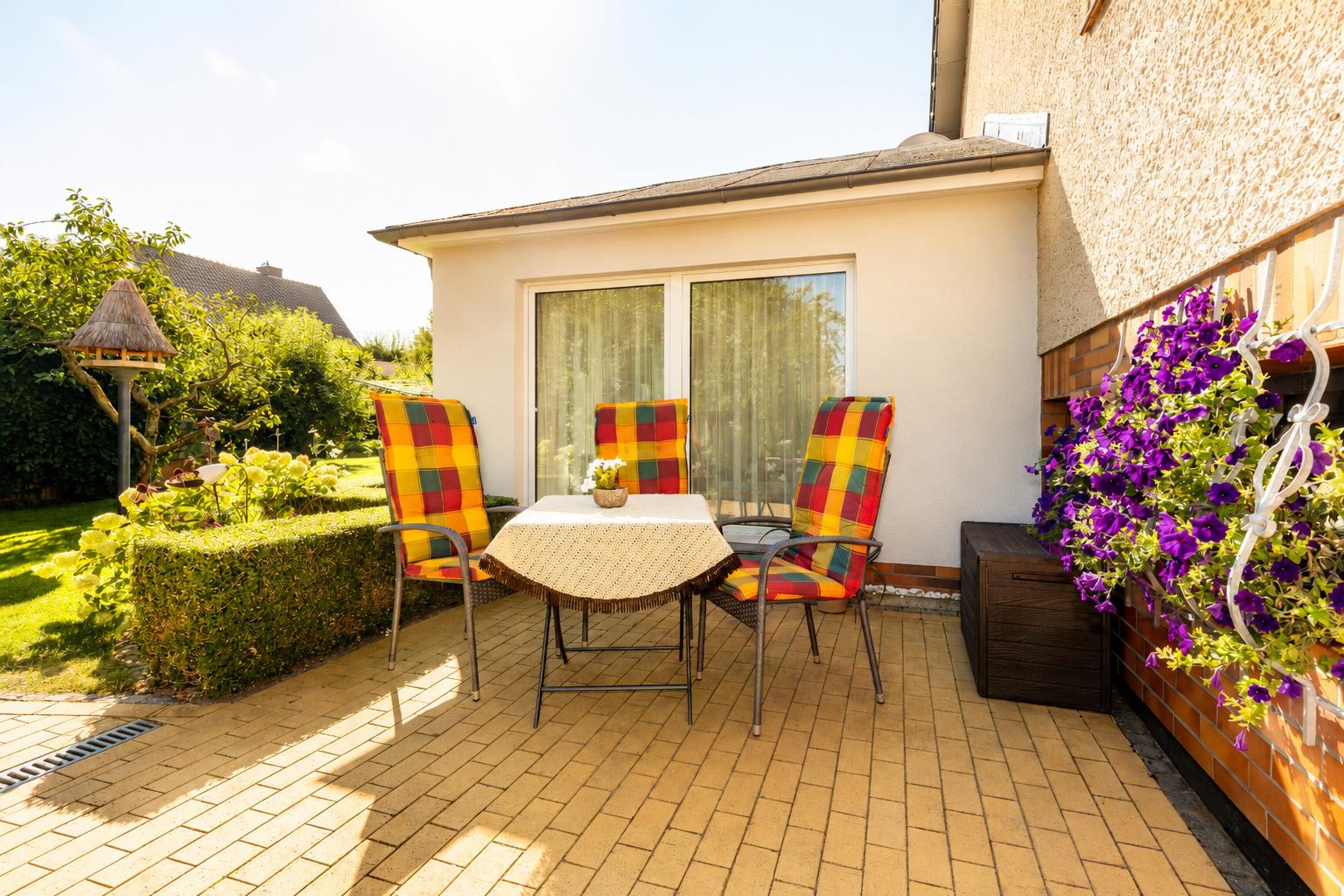 Terrasse mit Tisch und drei Stühlen, Blumenkasten und Garten im Hintergrund.