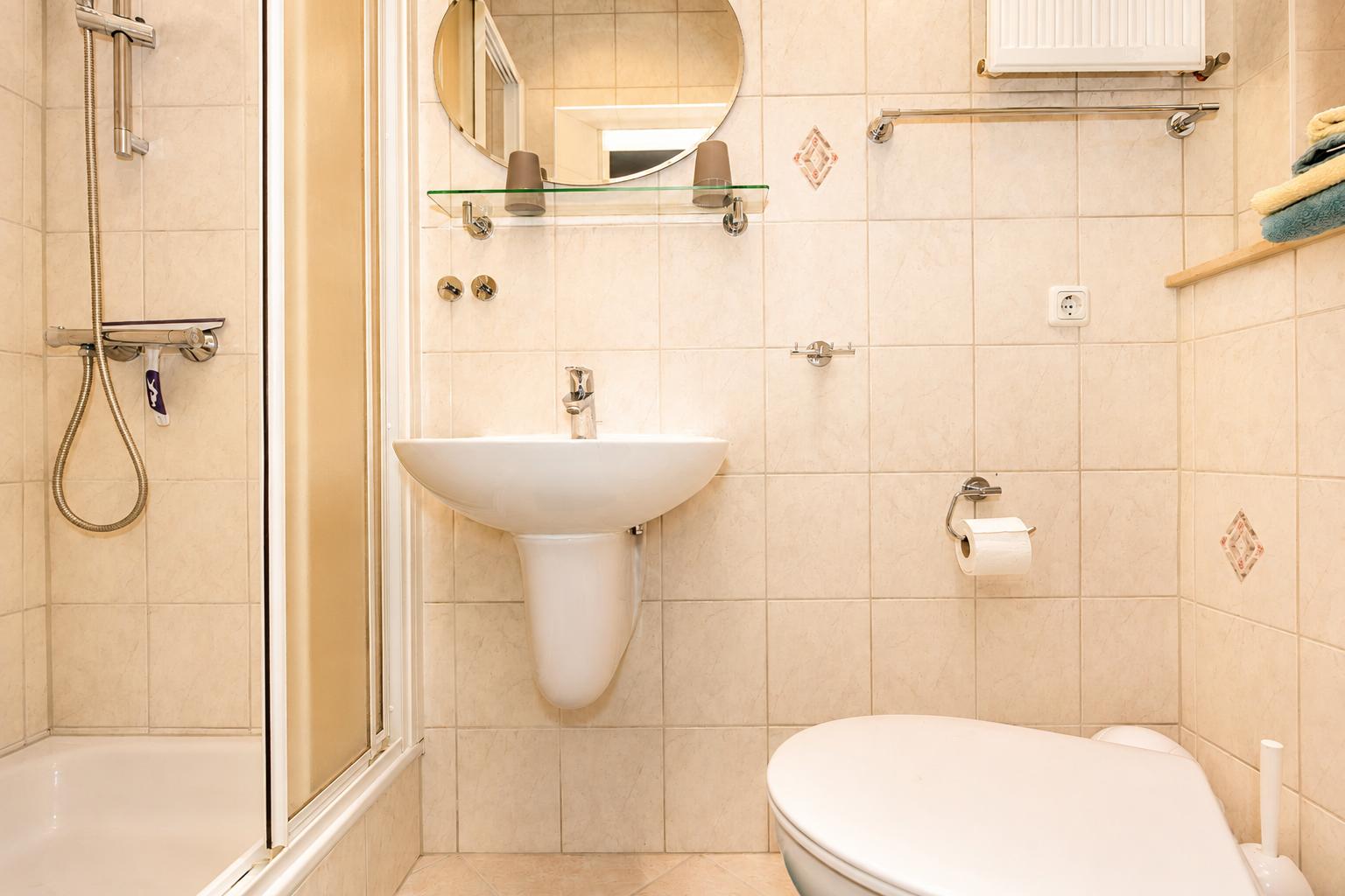 Badezimmer mit Dusche, Waschbecken und Toilette. Fliesenwand und Spiegel.