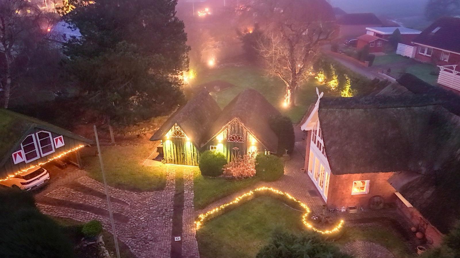 Dorfhaus mit strohgedeckten Dächern und Beleuchtung im Garten