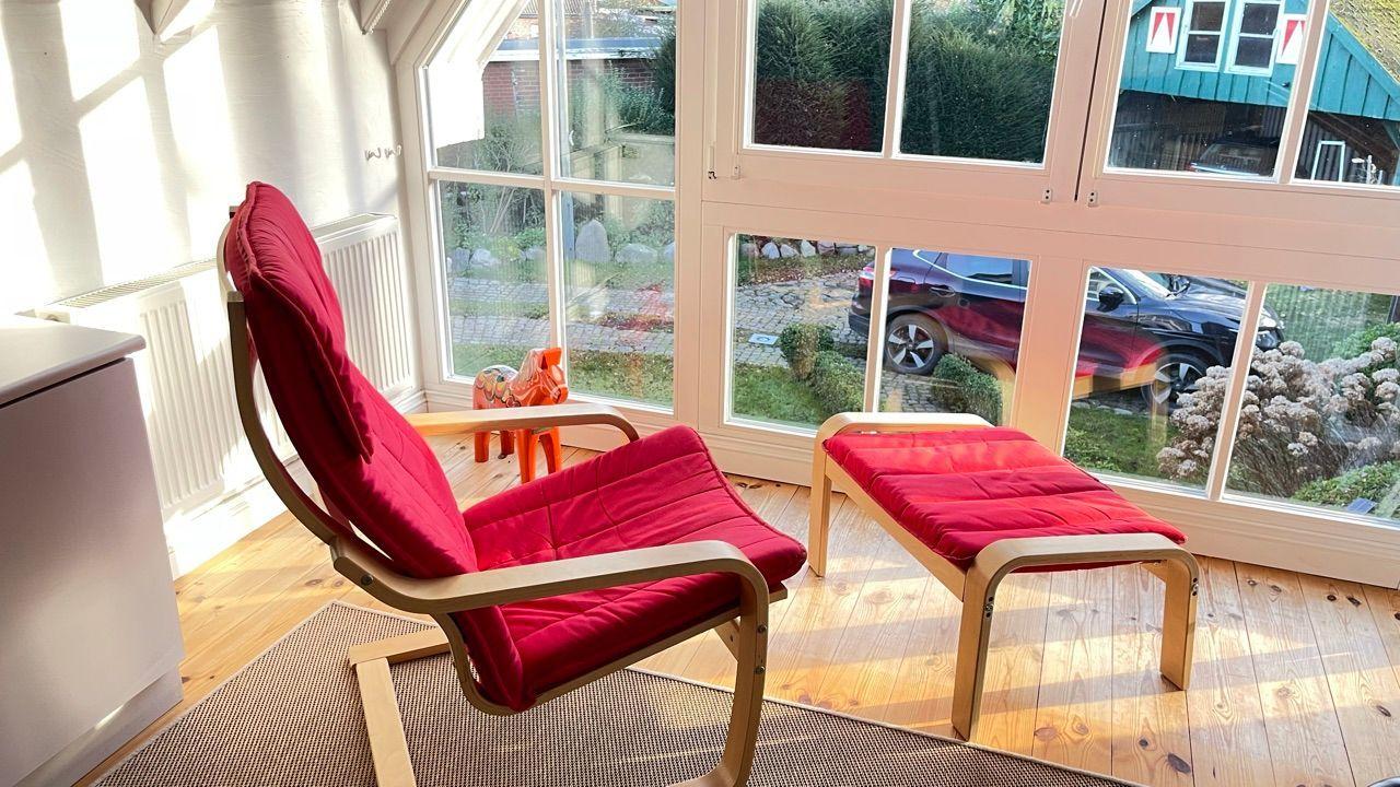 Roter Sessel und Hocker vor großen Fenstern mit Blick auf Garten und Hof.