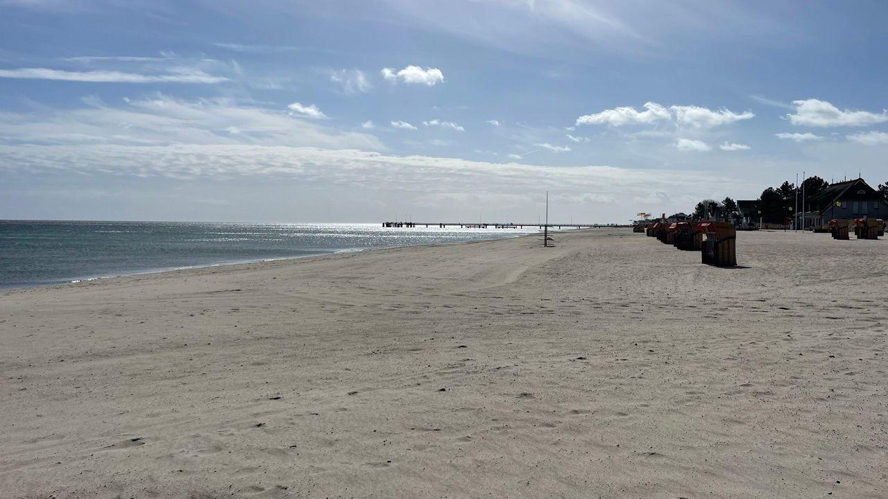 Strand mit Sand, Meer und Strandkörben. Im Hintergrund liegt eine Promenade.