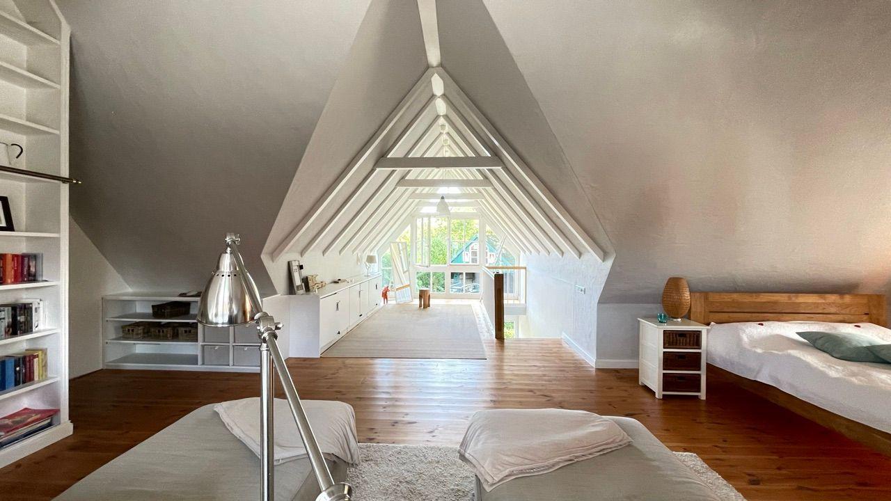 Schlafzimmer mit Dachschrägen, Holzboden und Blick auf Balkon