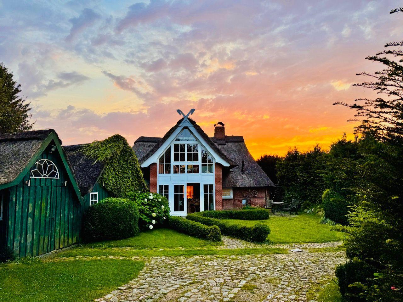 Haus mit Strohdach und Gartenweg bei Sonnenuntergang.