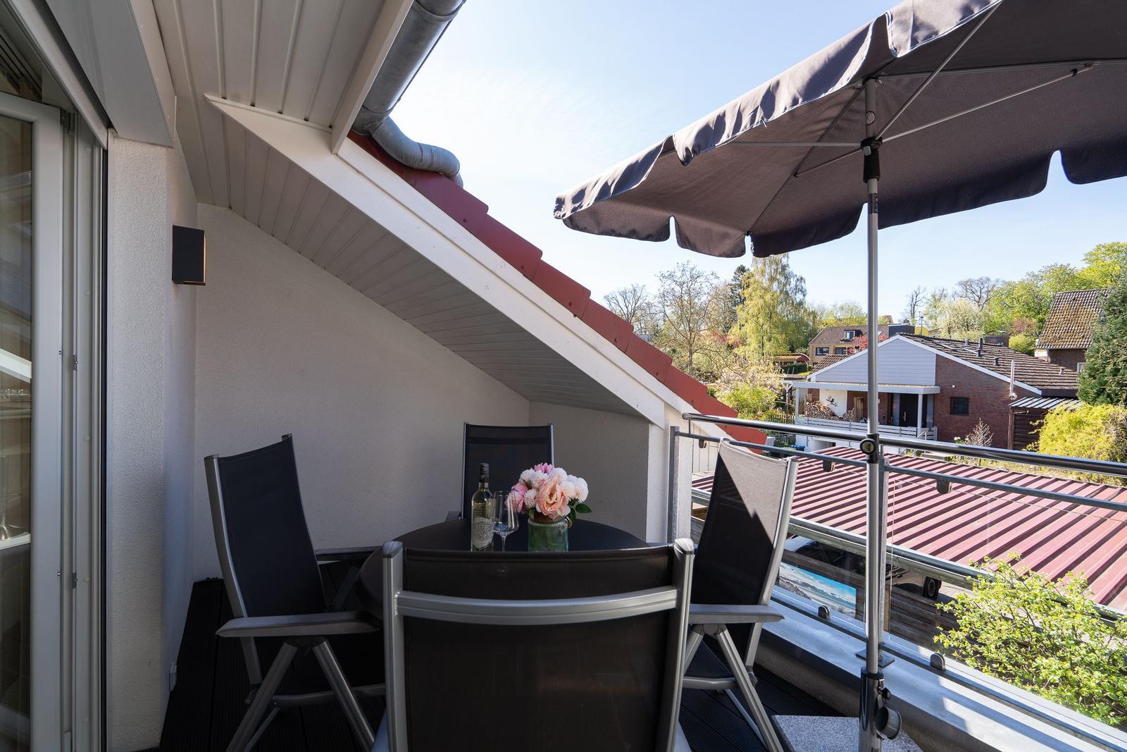 Terrasse mit Tisch, Stühlen und Sonnenschirm. Blick auf Dächer und Bäume.