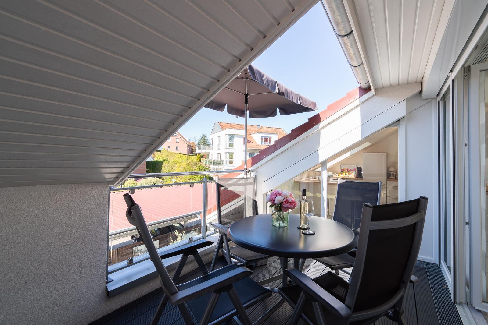 Terrasse mit Tisch, Stühlen und Sonnenschutz. Blick auf Dächer und Grünflächen.