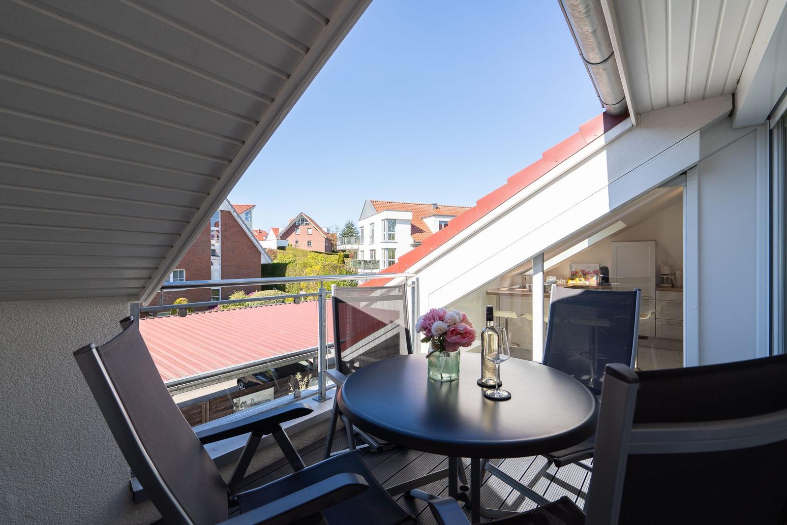 Terrasse mit Tisch, Stühlen und Blumen. Blick auf rote Dächer und Wohnhäuser.