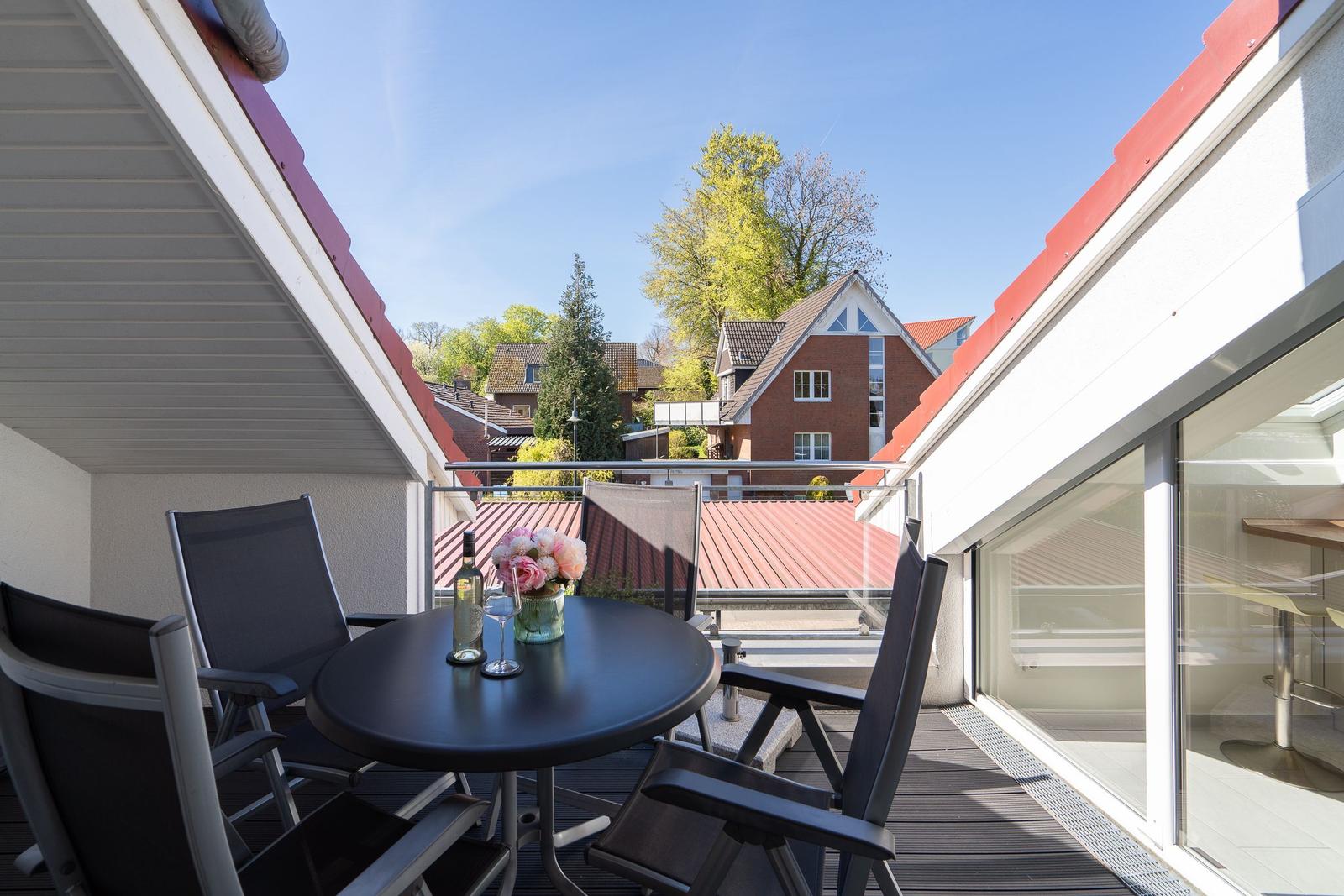 Terrasse mit Tisch und Stühlen, Blick auf rote Dächer und Bäume.
