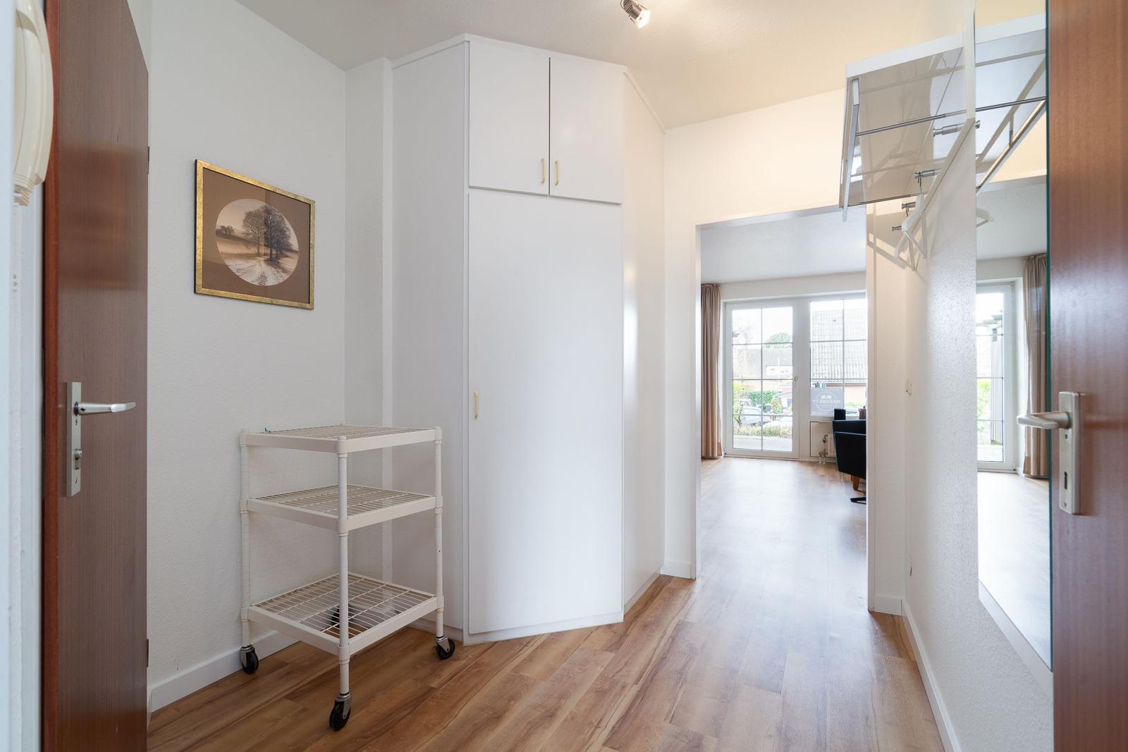 Hallway with wardrobe, rolling cart, and view into living area with windows.