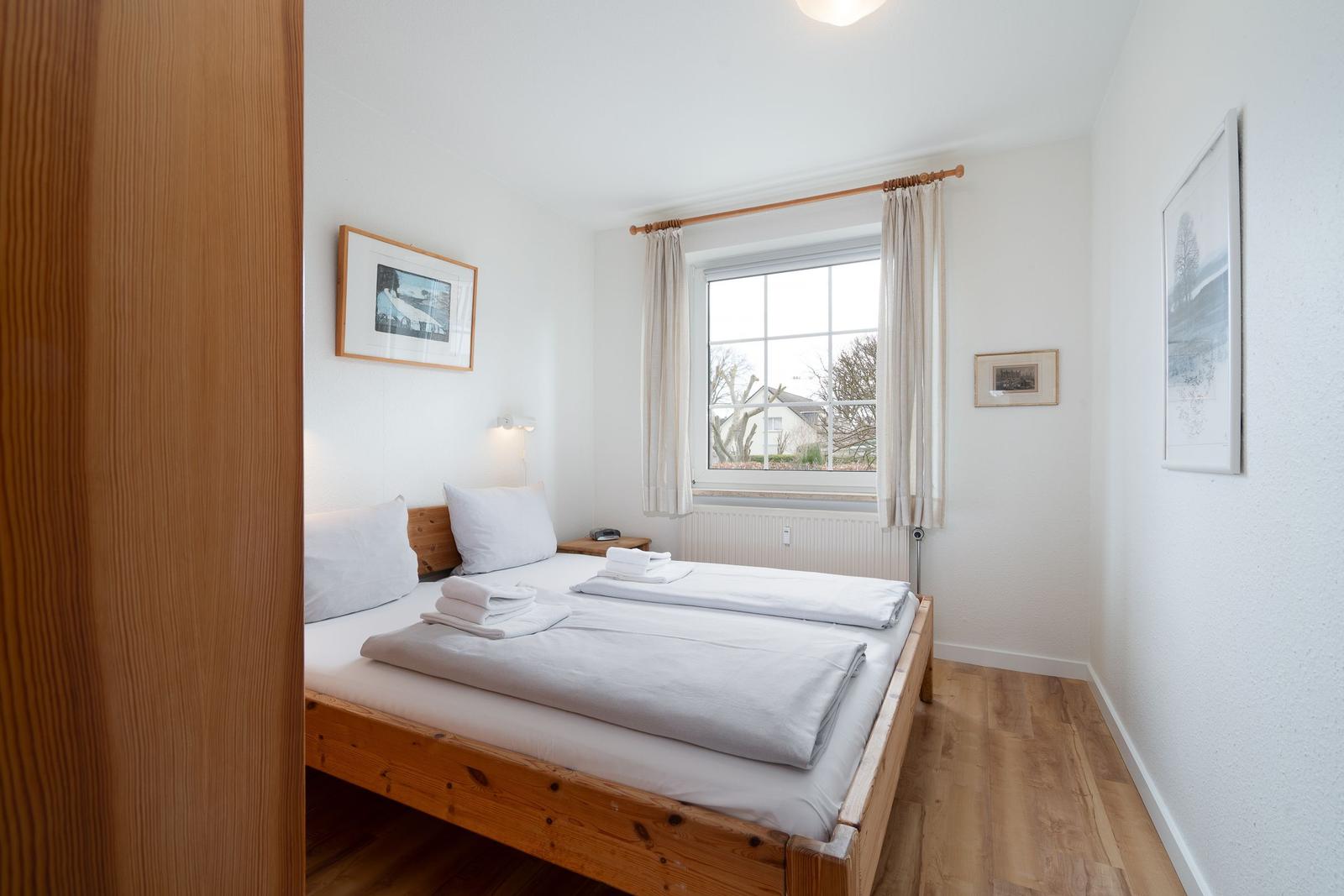 Bedroom with wooden bed, window, and pictures on the walls.