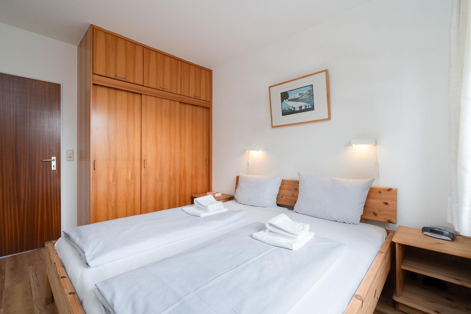 Room with double bed, wooden closet, and nightstand. Wall art and lighting.