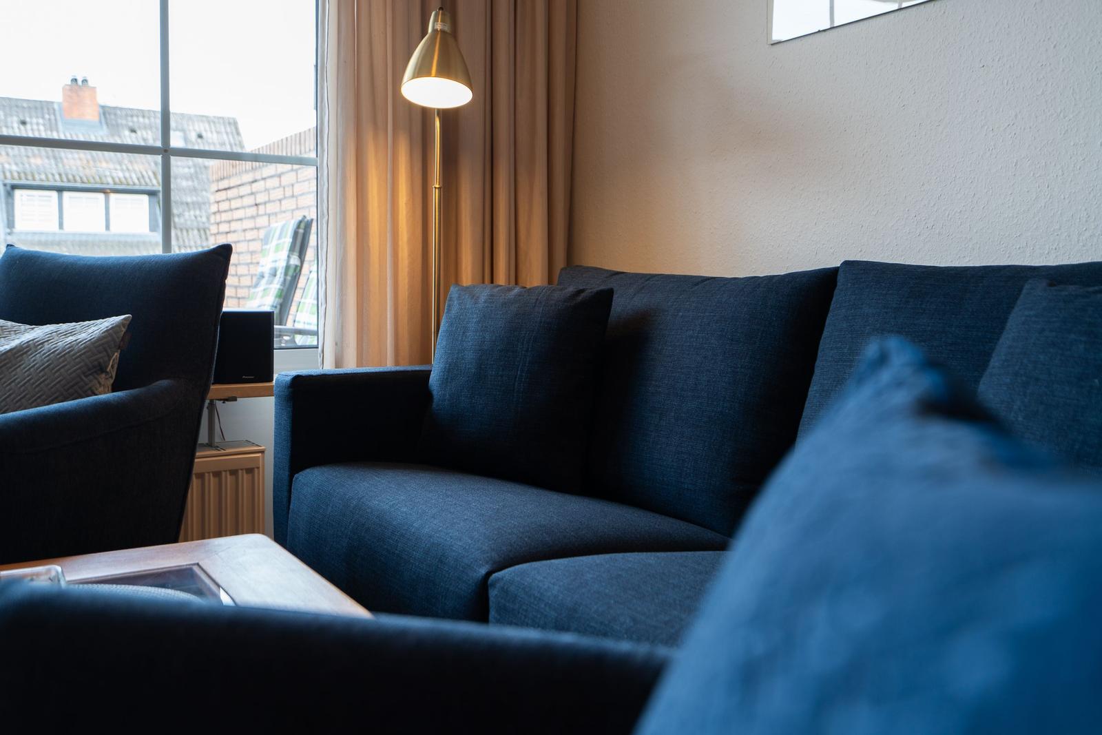 A living room with blue sofa, floor lamp, and window view of buildings.