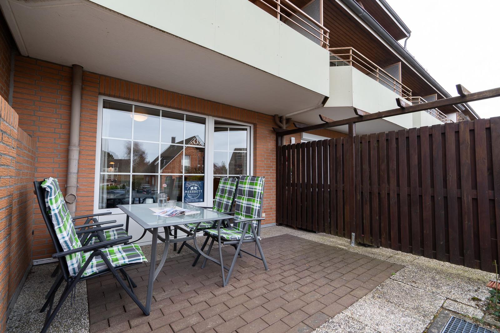 Terrace with table and chairs in front of an apartment with windows and wooden fence.