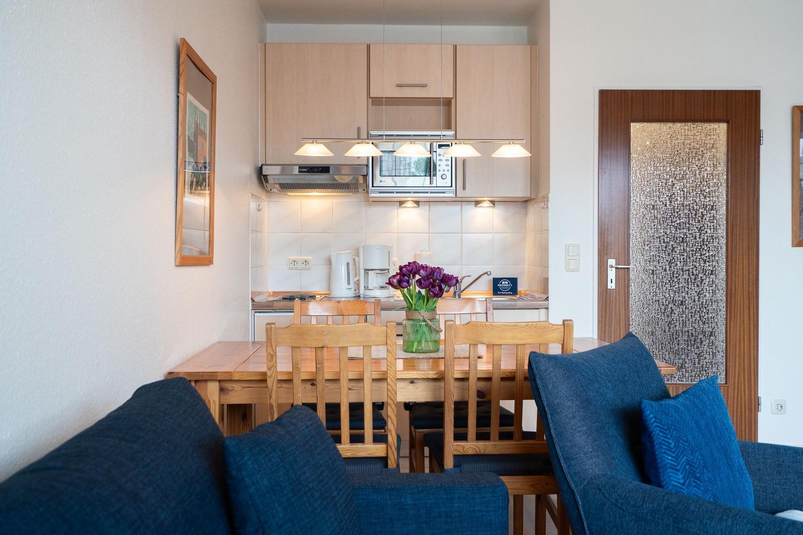 Kitchen with dining area, wooden table, chairs, and sofa with cushions.