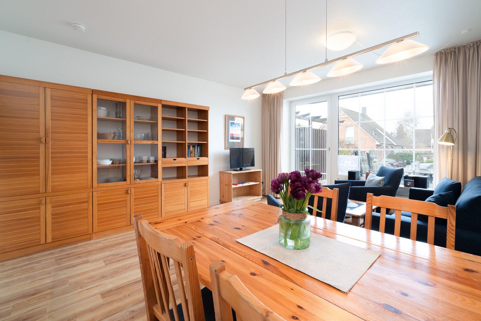 Dining area with wooden table, chairs, and kitchen cabinets. Passage to living room with sofa and window.