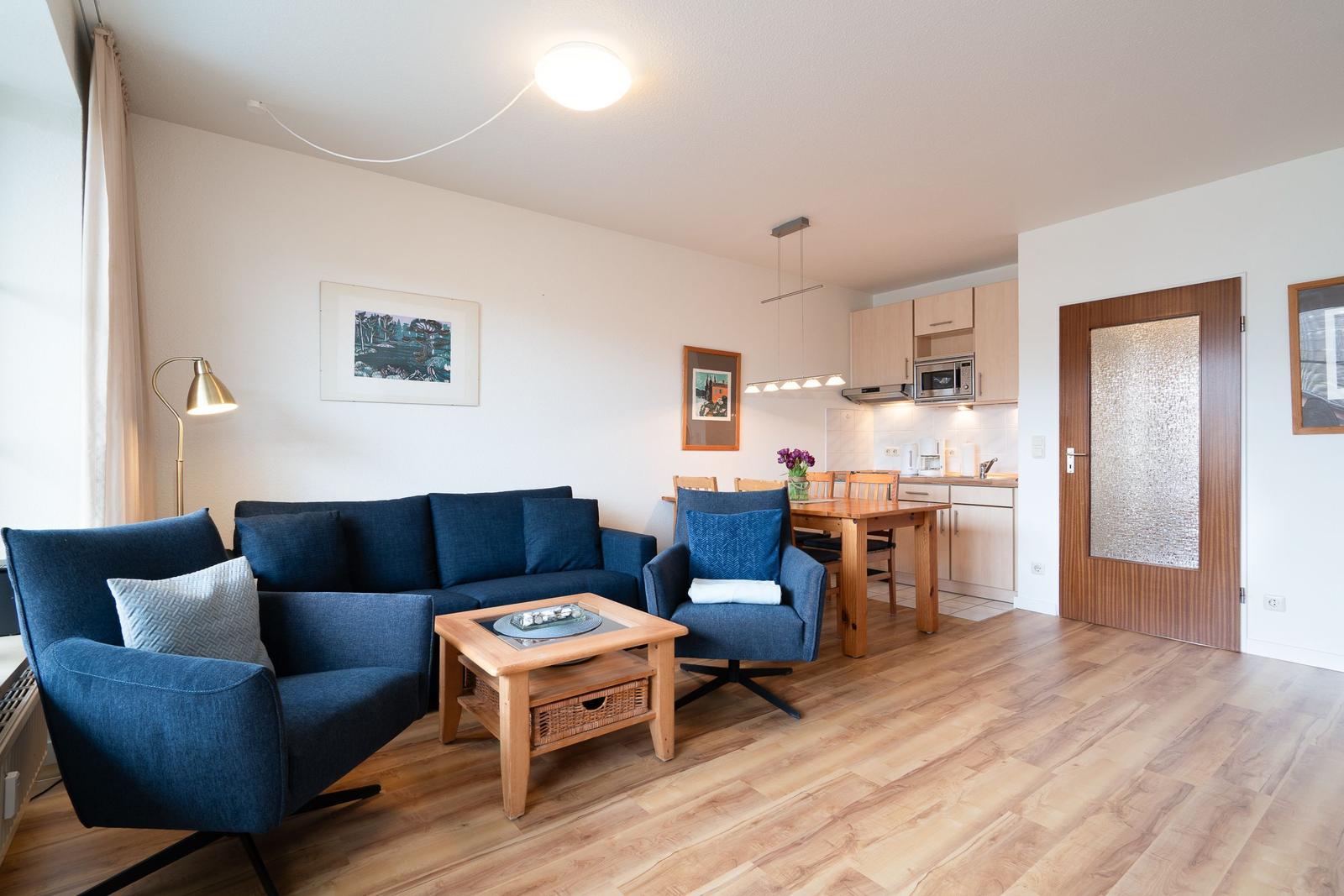 Living and dining area with kitchen, blue seating, and wooden floor.