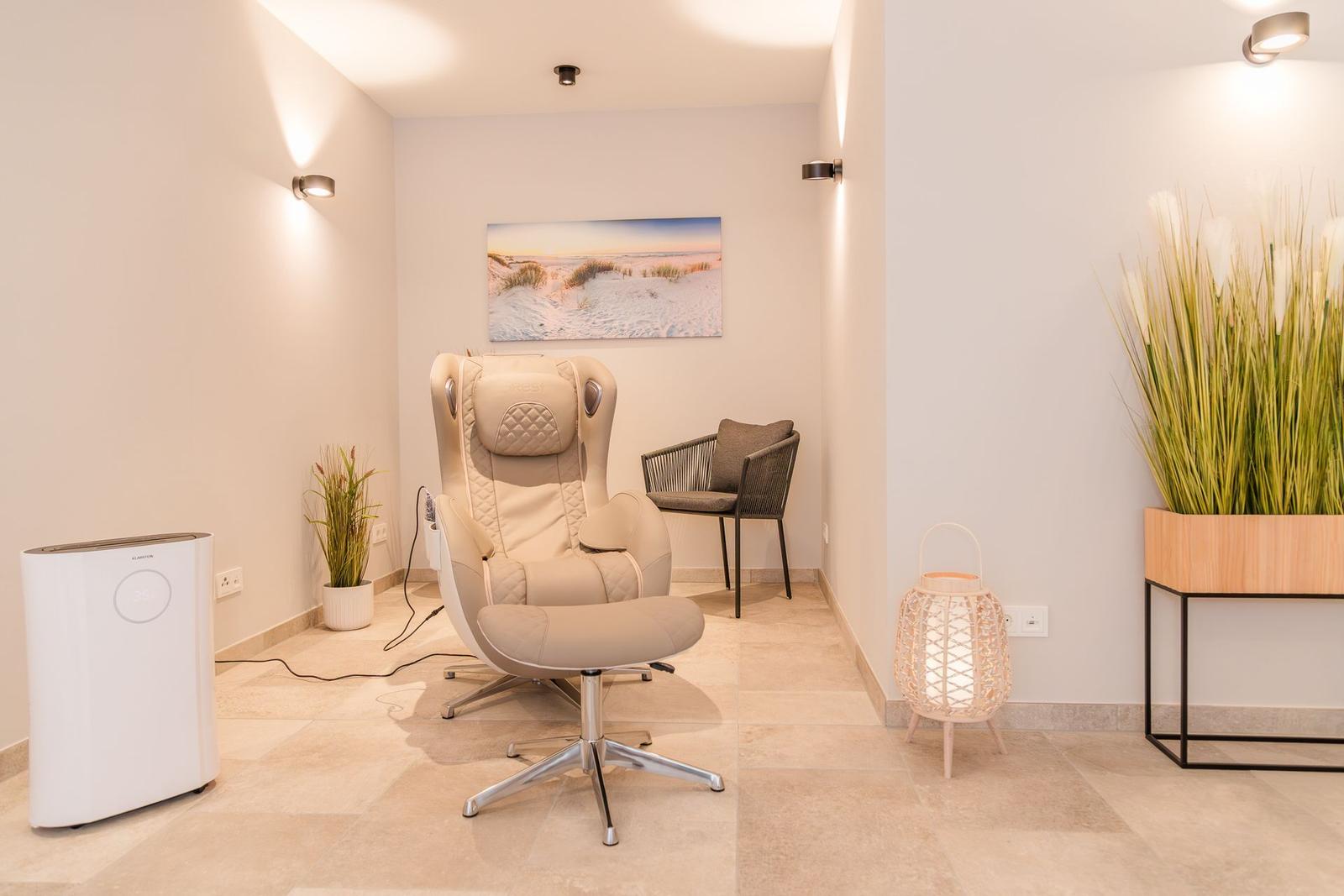 Raum mit Massagestuhl, kleiner Sessel, Pflanzen und Wandbild.