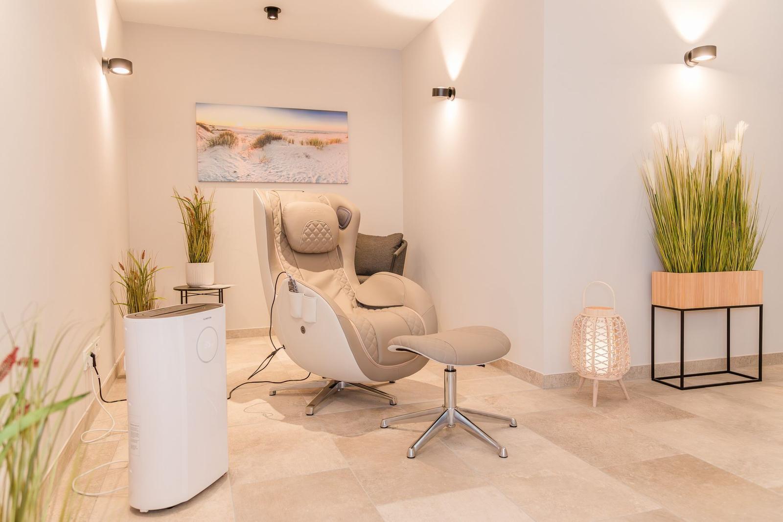 Massagestuhl mit Fußstütze, Wandbild, Pflanzen und Beleuchtung.