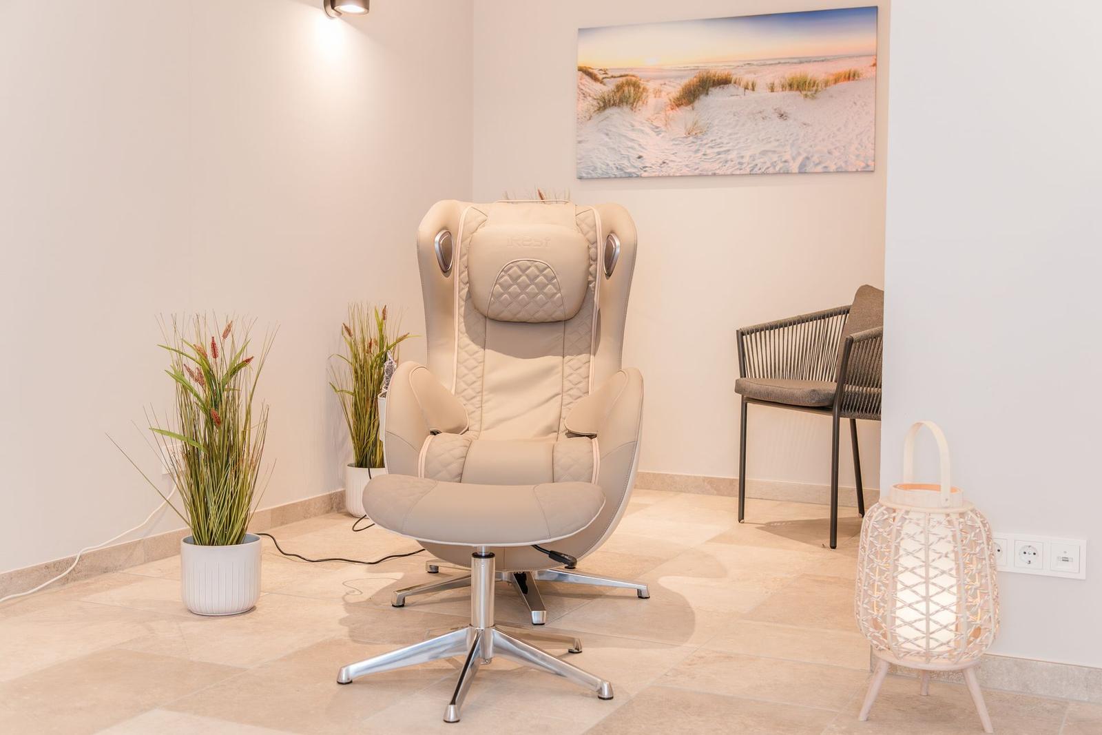Massagesessel mit Fußstütze, Pflanzen und Wandbild im Raum.
