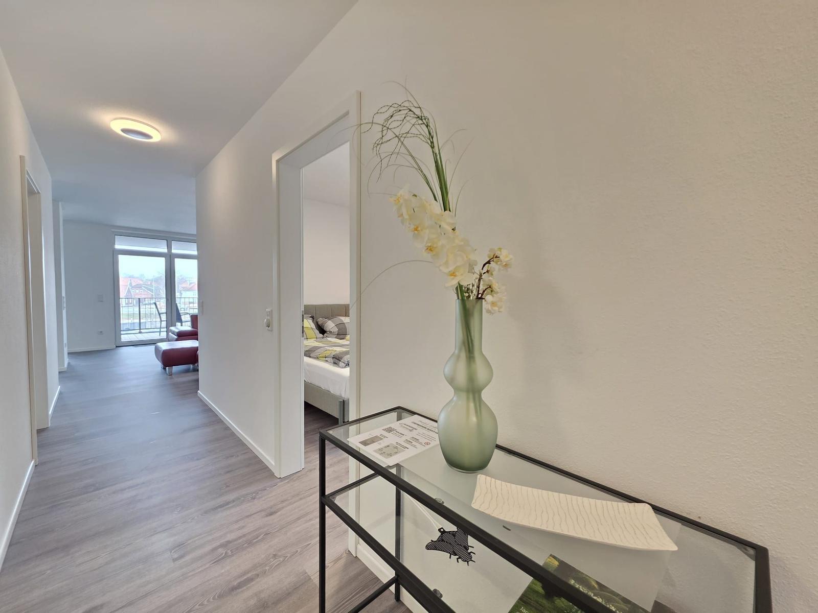Hallenflur mit Glasvitrine und Blumenvase. Blick in Schlafzimmer und Wohnbereich mit Balkon.