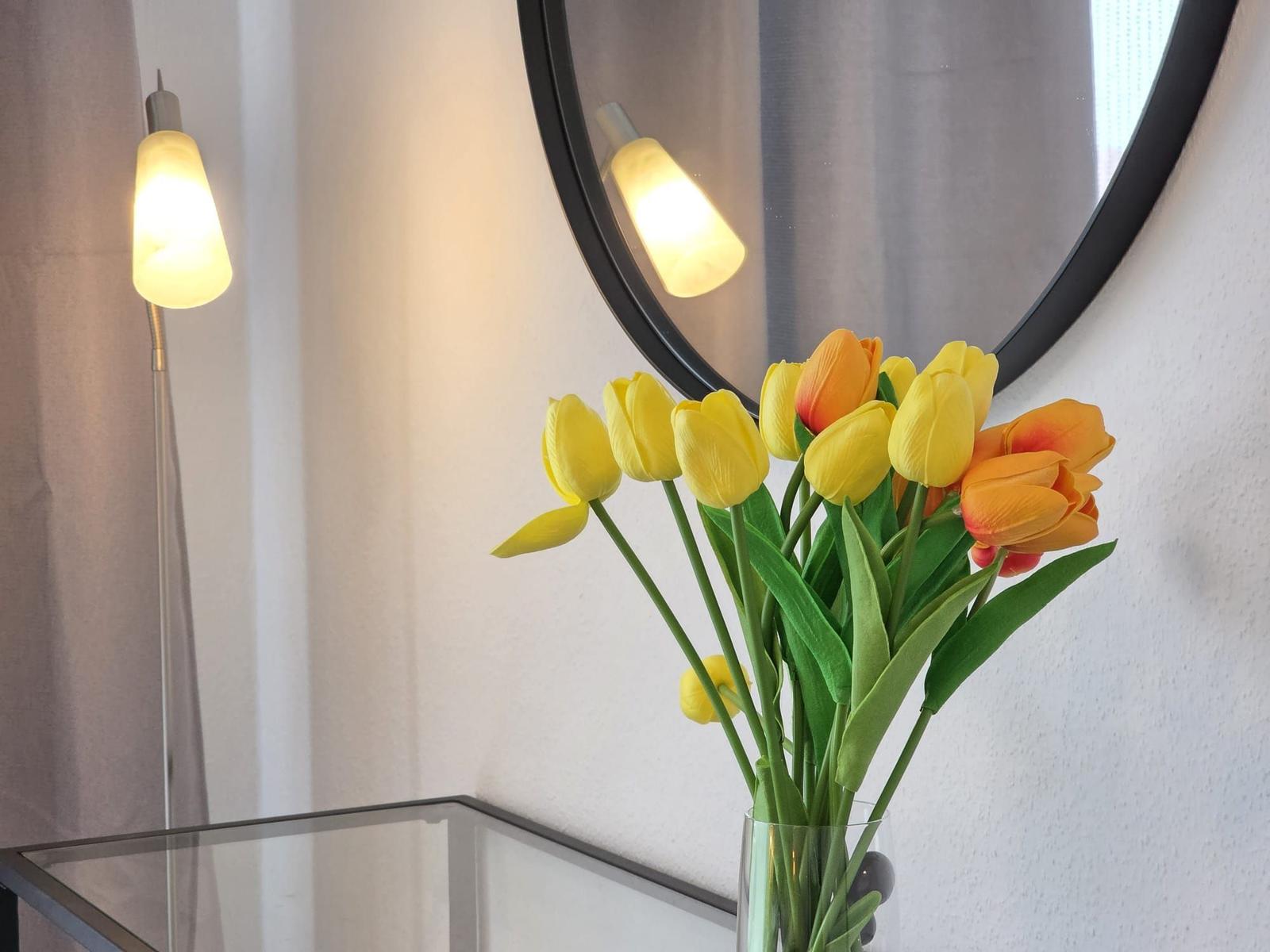 Tulpen in einem Glas auf einem Tisch vor einem Spiegel und einer Stehlampe.