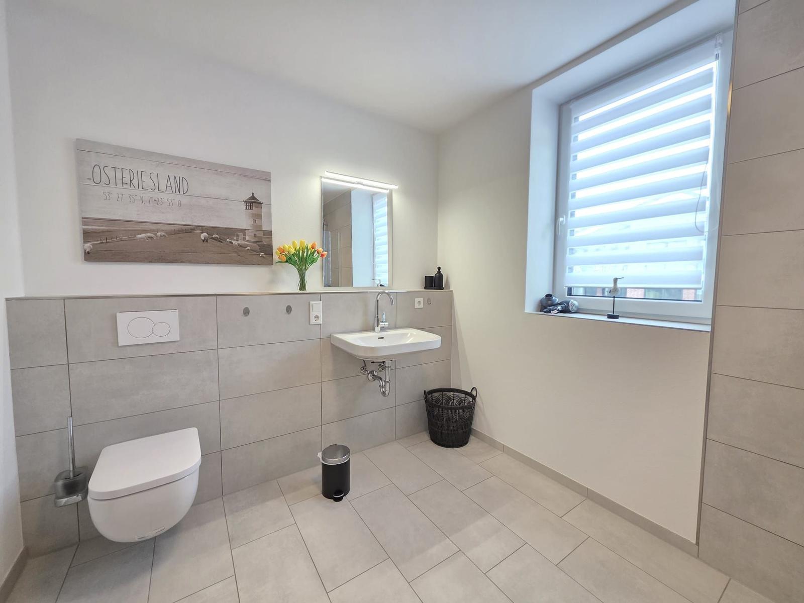 Badezimmer mit Toilette, Waschbecken und Fenster mit Jalousie.