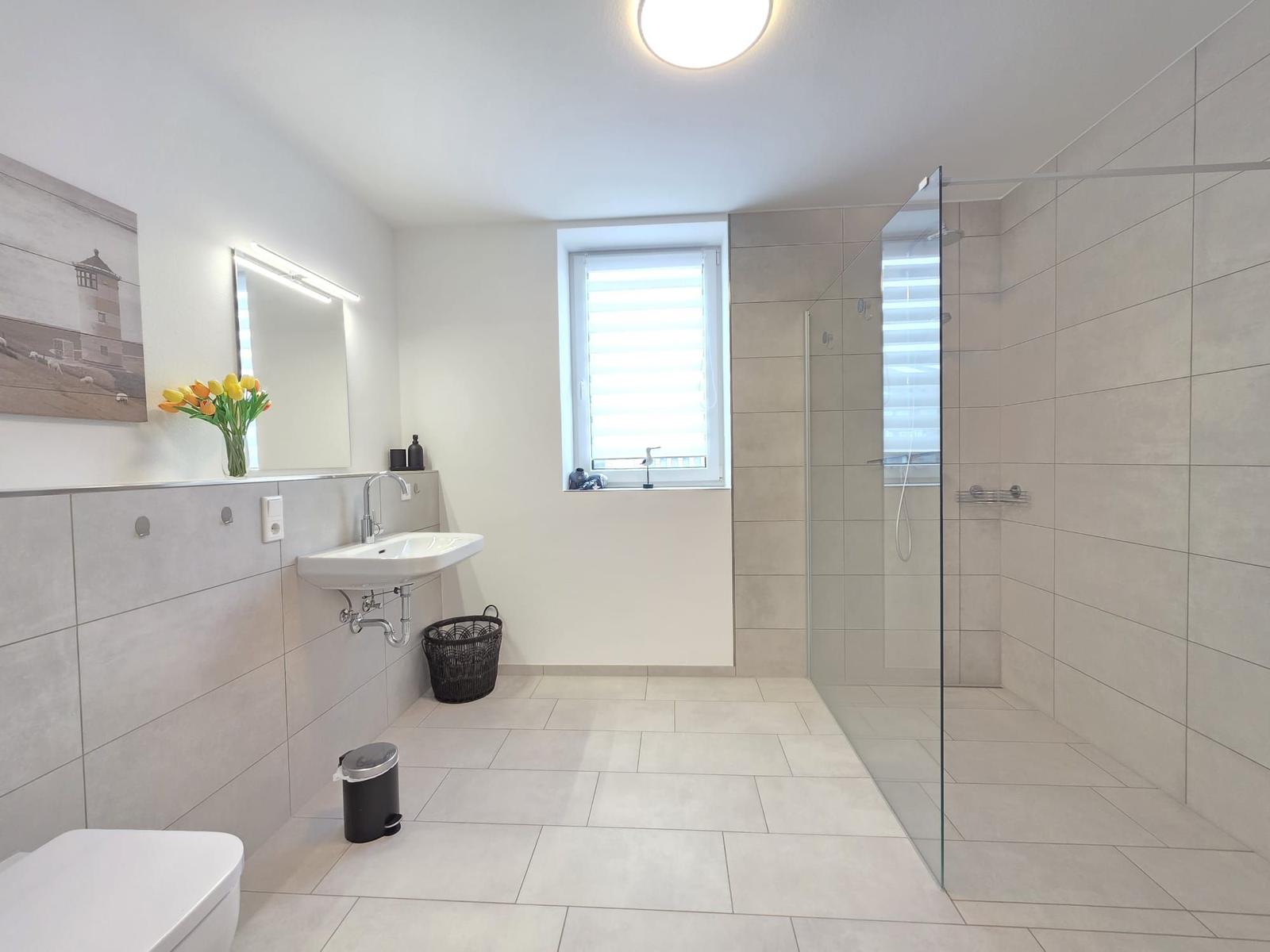 Badezimmer mit Dusche, Waschbecken und Toilette. Fenster mit Jalousie.