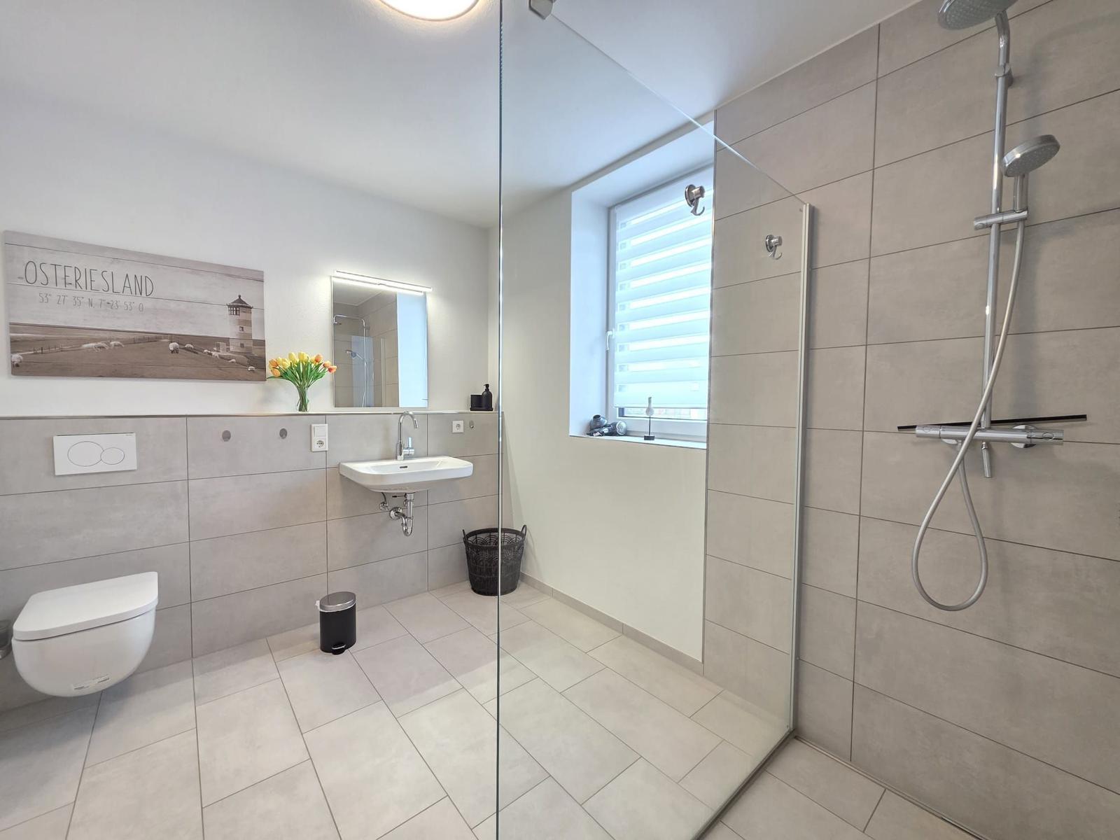 Badezimmer mit Dusche, Waschbecken und Toilette. Fenster mit Jalousie.