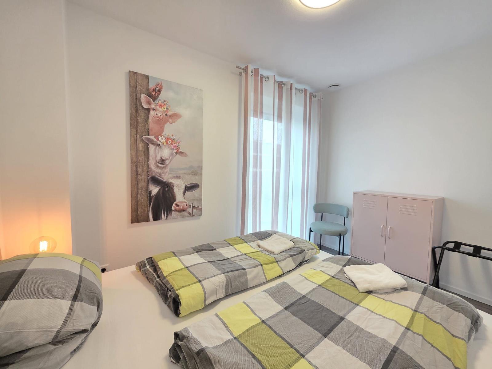 Zimmer mit zwei Betten, Wandbild und Gardinen.