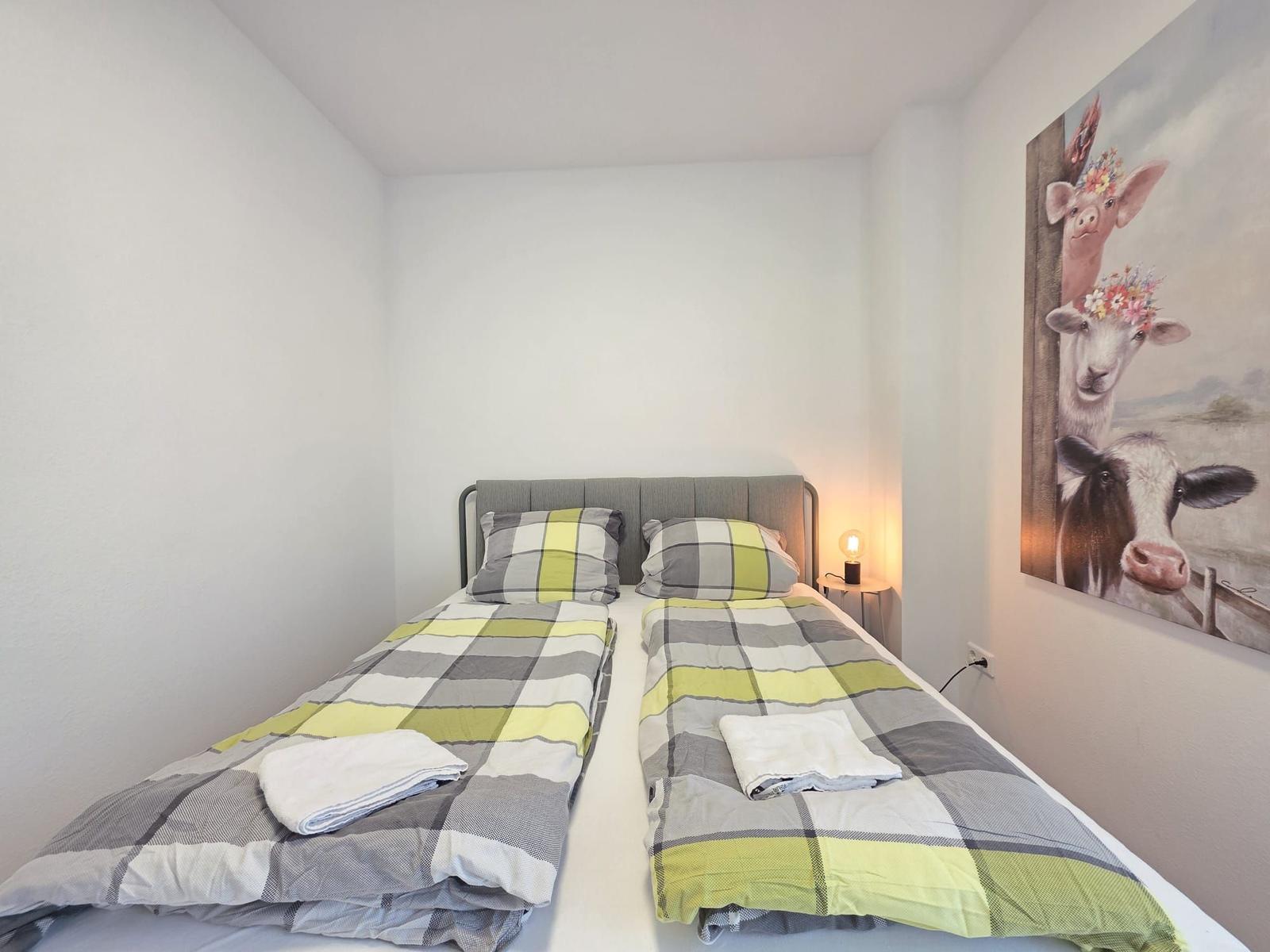 Zimmer mit Doppelbett, gemustertem Bettwäsche und Wandbild mit Tieren.