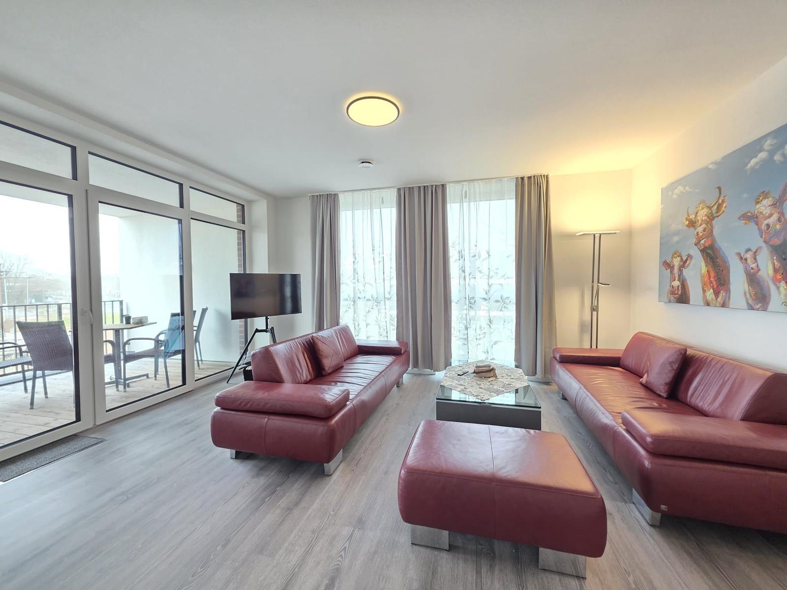 Wohnzimmer mit zwei roten Ledersofas, Glas-Tisch und Balkonzugang.
