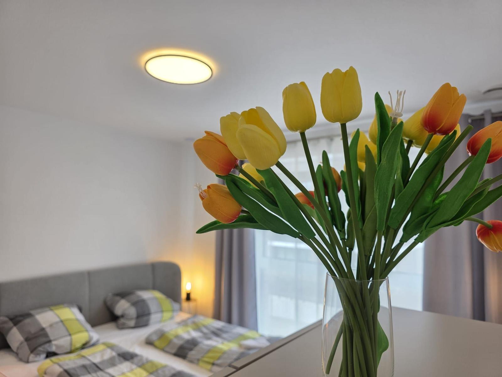 Ein Bett mit kariertem Bettzeug und eine Vase mit Tulpen im Vordergrund.