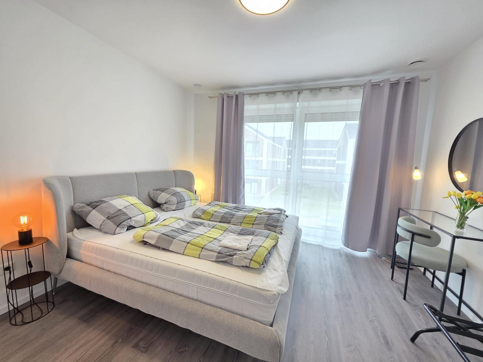 Schlafzimmer mit Bett, Schreibtisch und Balkonzugang.