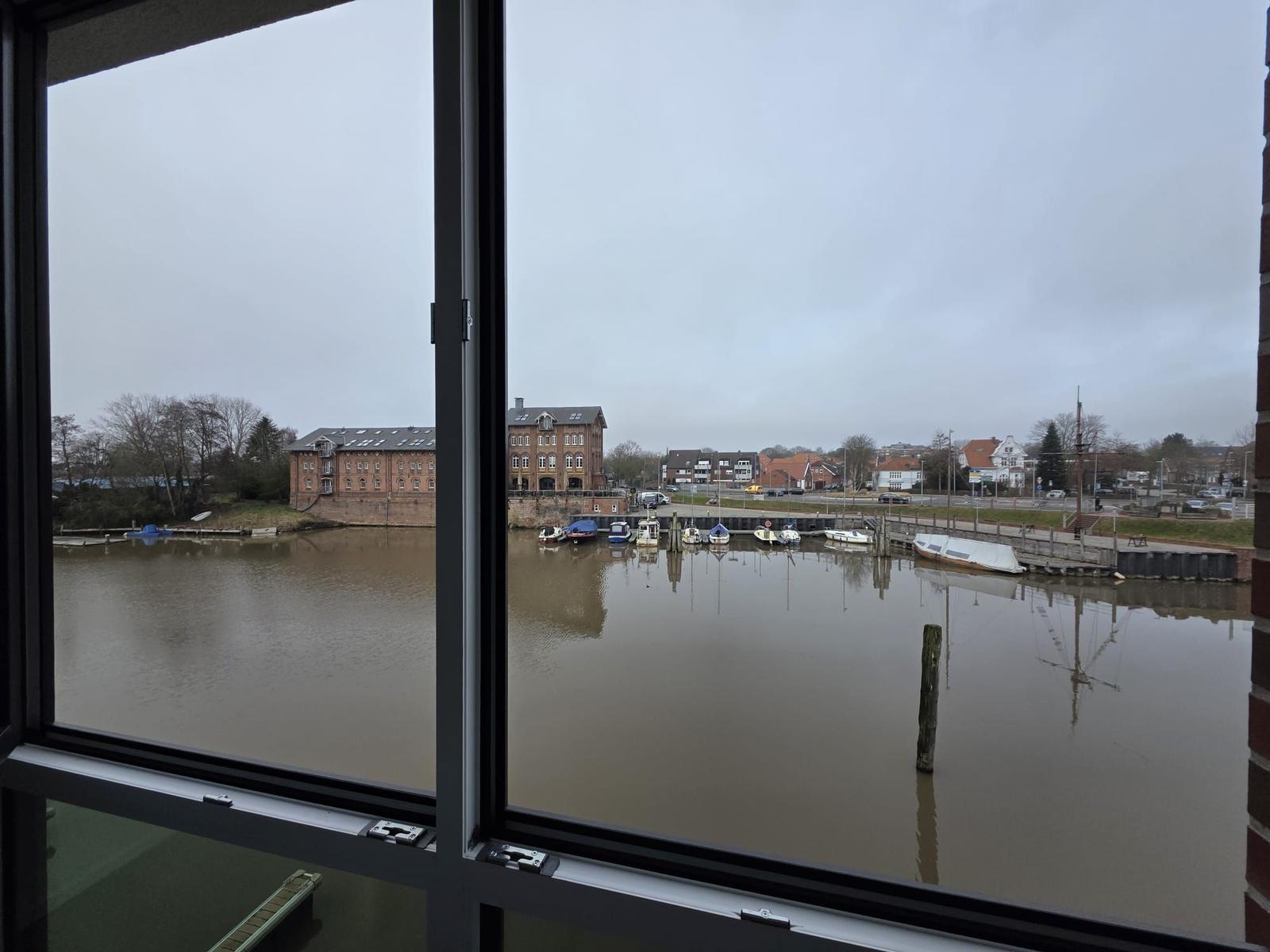 Blick auf Hafen mit Booten und gegenüberliegenden Gebäuden durch Fenster.