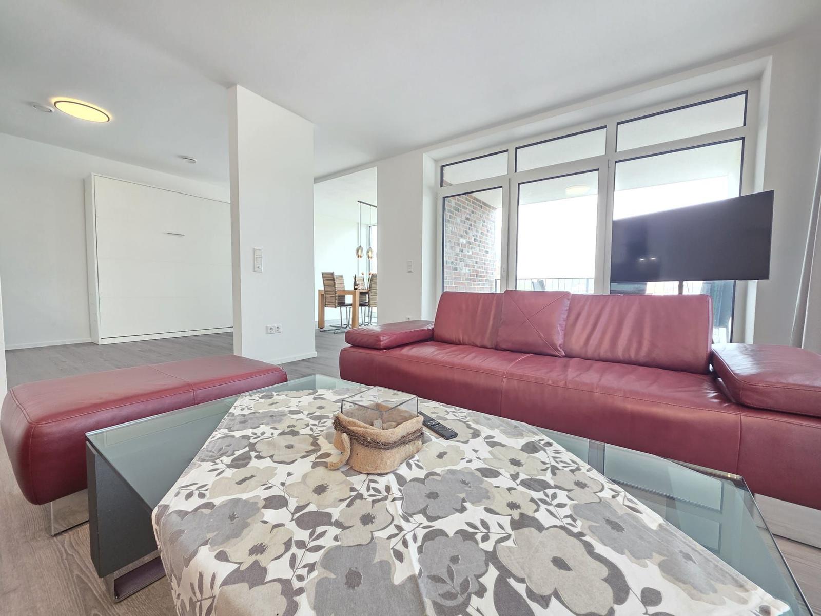 Ein Wohnzimmer mit rotem Sofa, Glas-Tisch und großen Fenstern.
