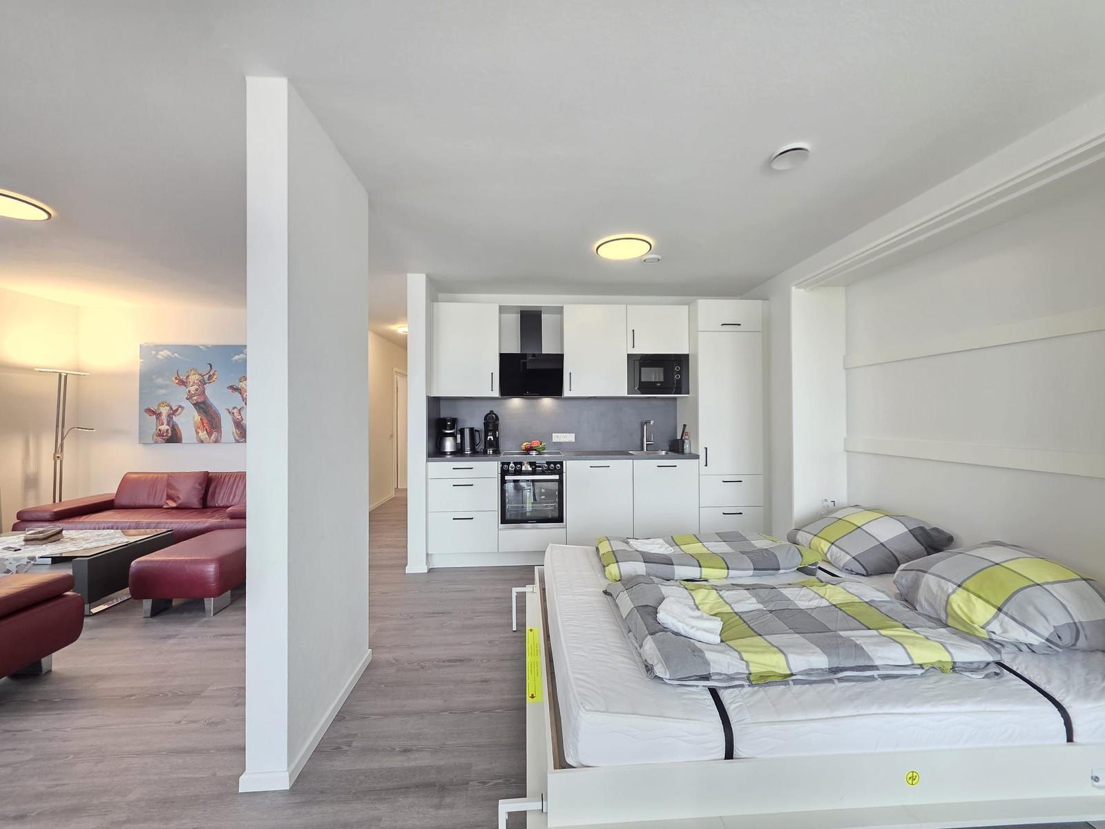 Schlafzimmer mit Bett, Küche und Wohnbereich mit rotem Sofa.