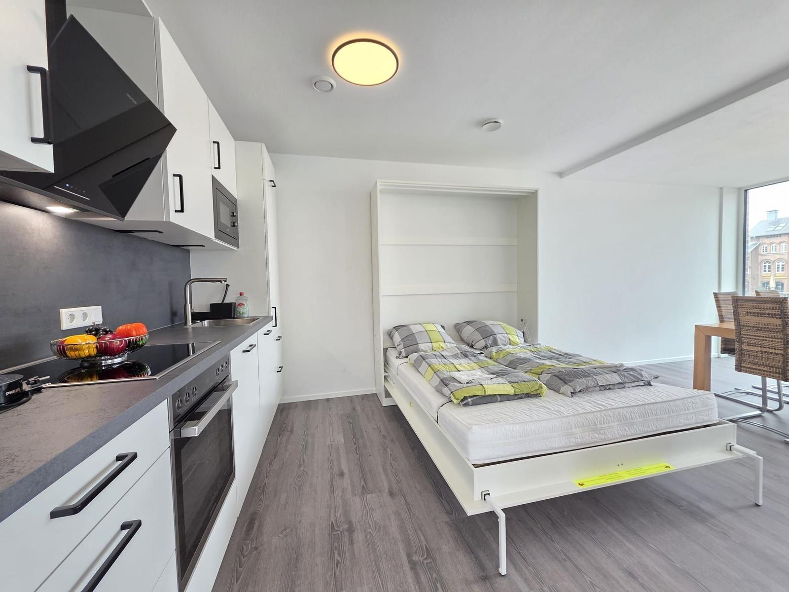 Küche mit Schlafgelegenheit. Bett im Schrank. Tisch mit Stühlen. Fensterblick.