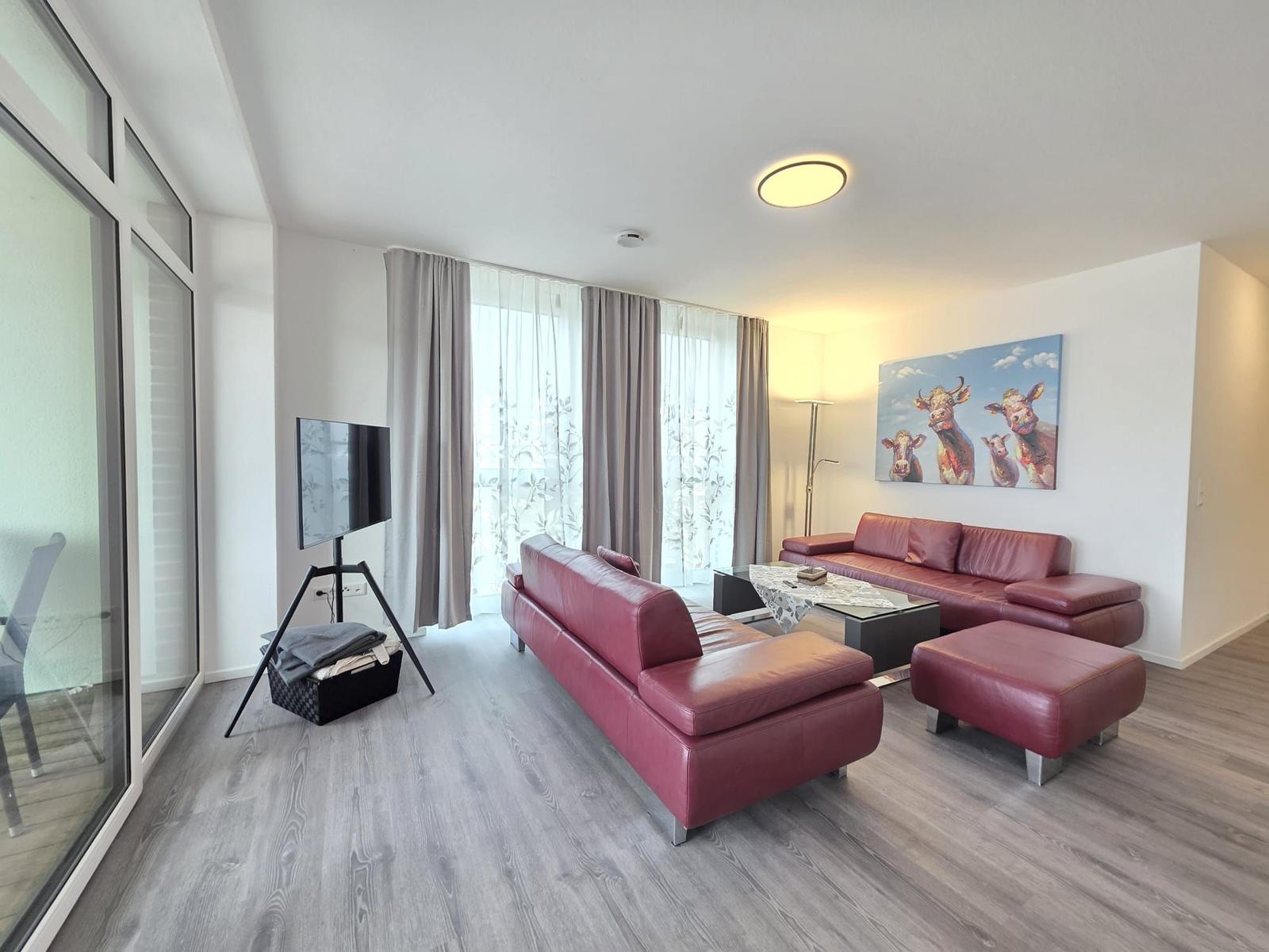 Wohnzimmer mit rotem Sofa, Glasfront und Wandbild mit Kühen.