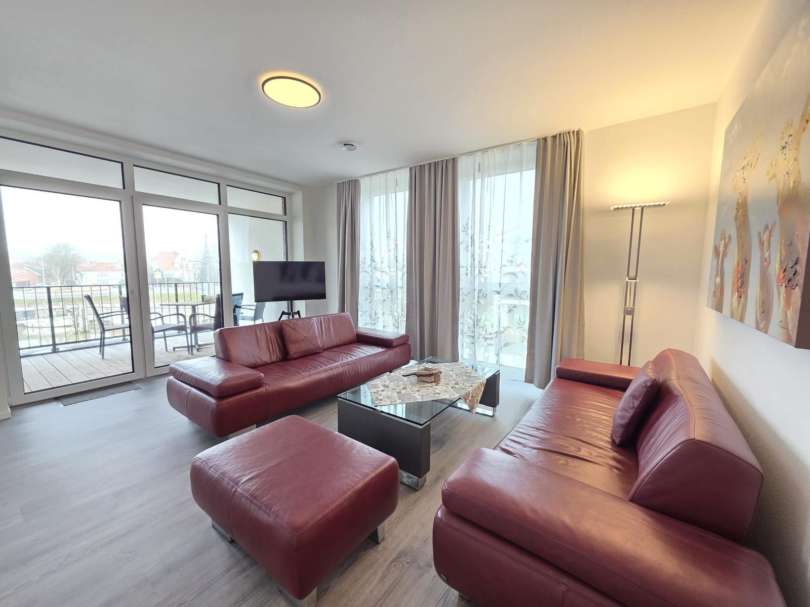Wohnzimmer mit zwei roten Ledersofas, Glas-Tisch und Balkonzugang.