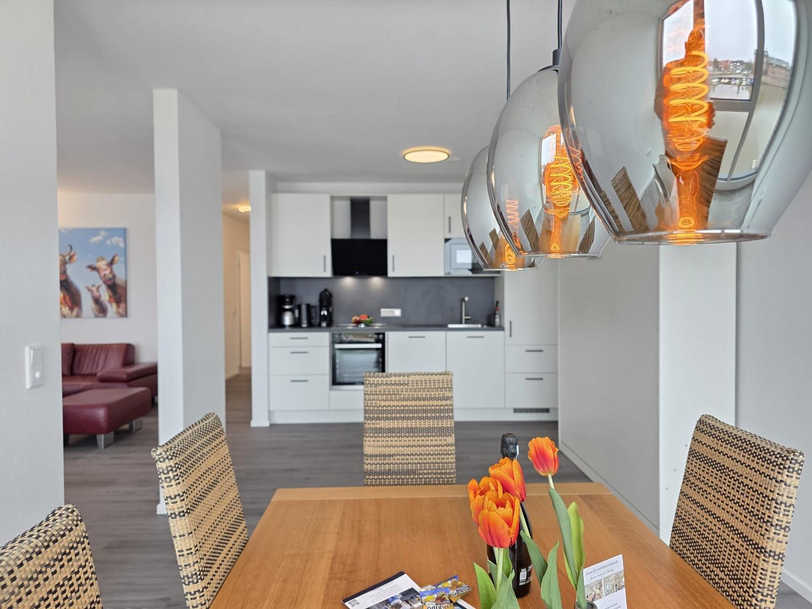 Essbereich mit Tisch, Stühlen und Tulpen. Küche und Wohnzimmer im Hintergrund.