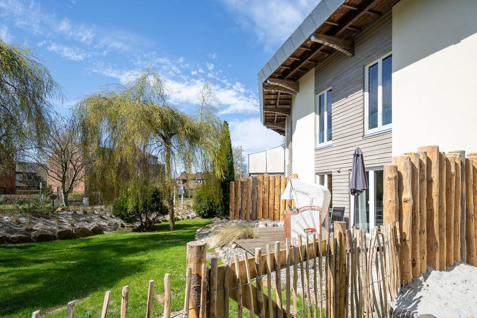 Haus mit Garten, Holzgeländer und Sitzgelegenheit unter einem Sonnenschirm.