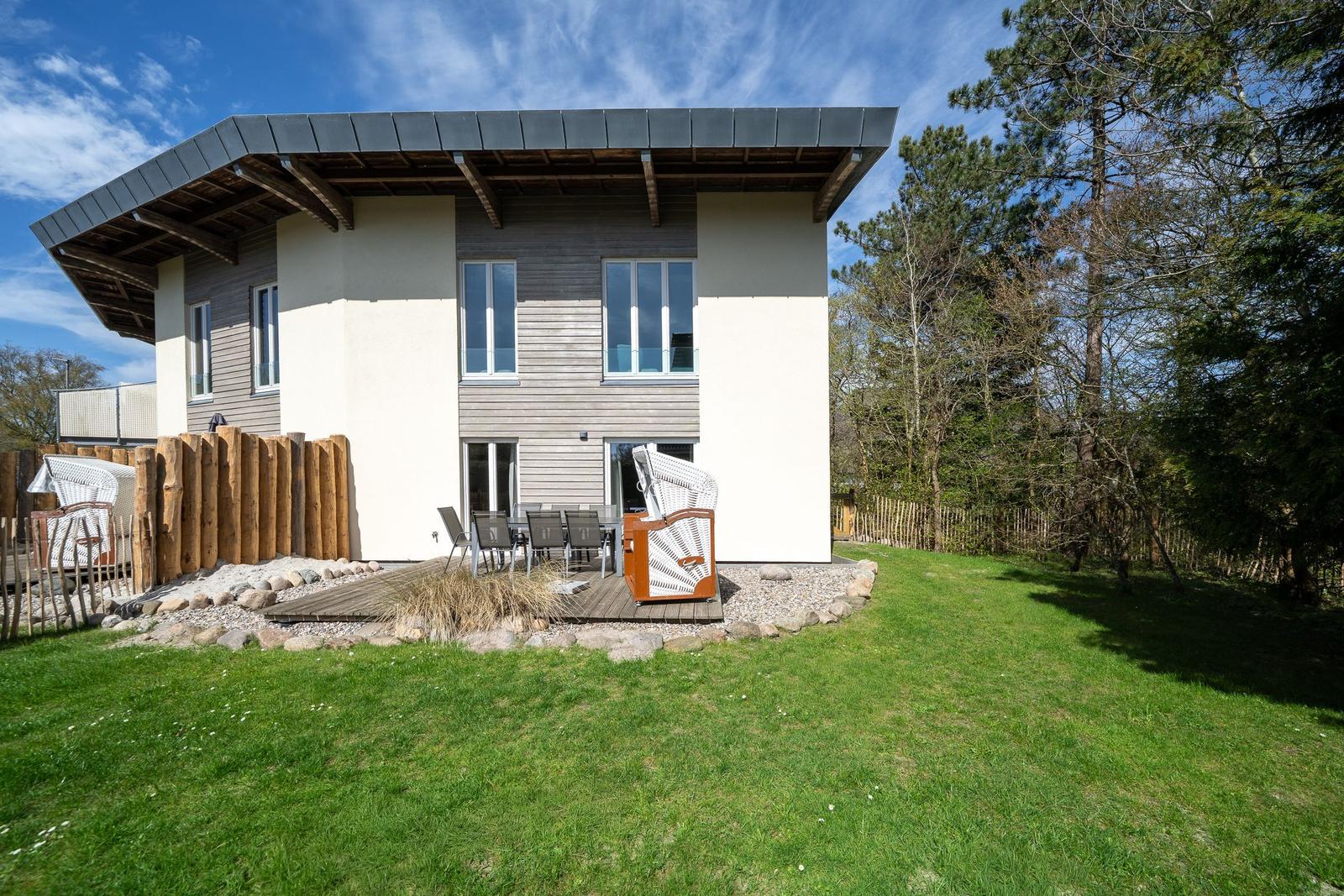 Moderne Villa mit Terrasse und Garten. Holzgeländer und Bäume umgeben das Haus.