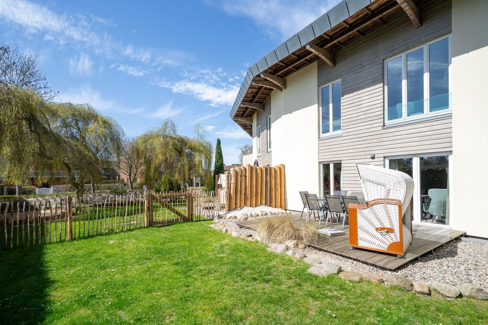 Haus mit Terrasse, Garten und Sitzgelegenheiten unter blauem Himmel.