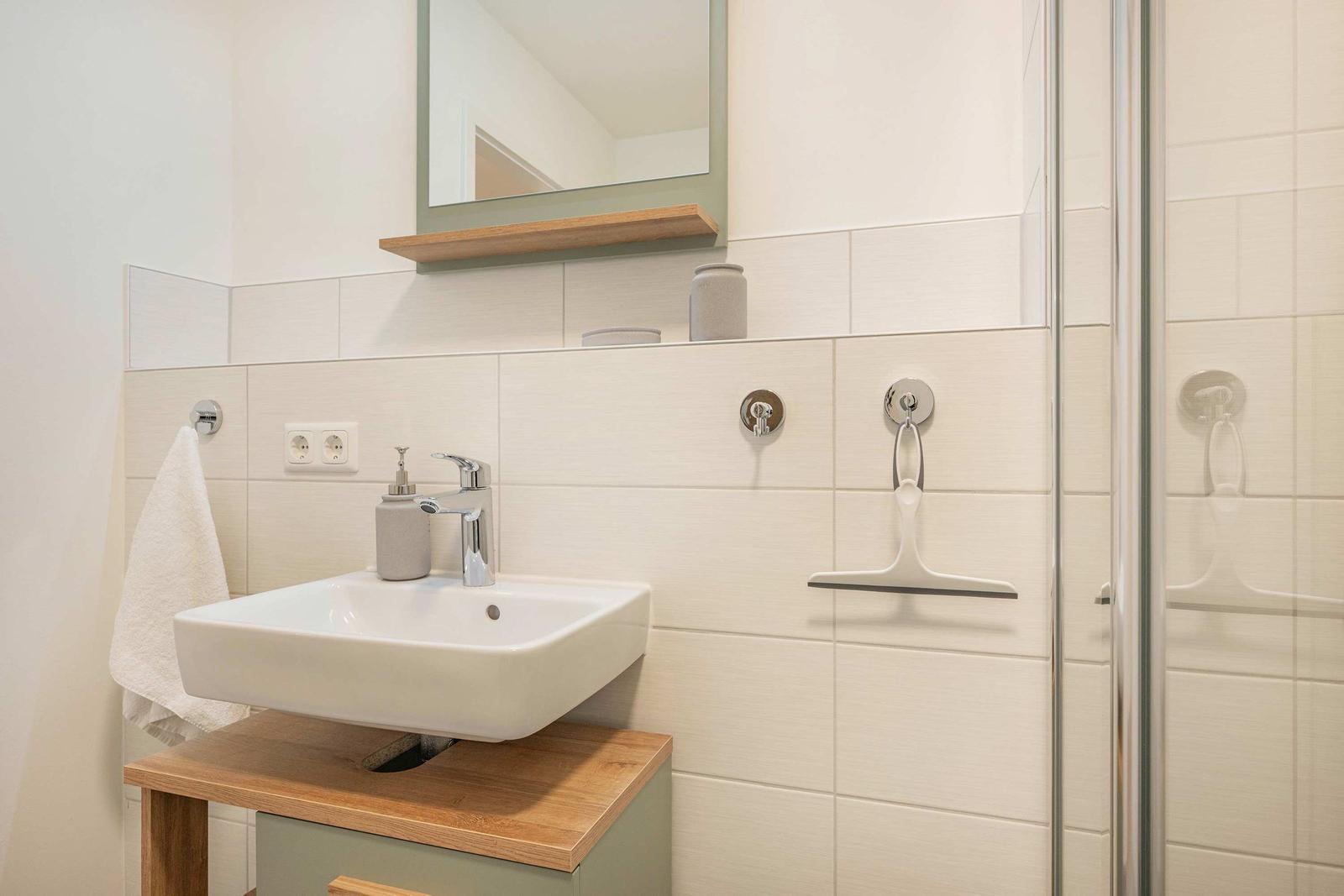 Bad mit Waschbecken, Spiegel und Dusche. Holzoberfläche und weiße Fliesen.
