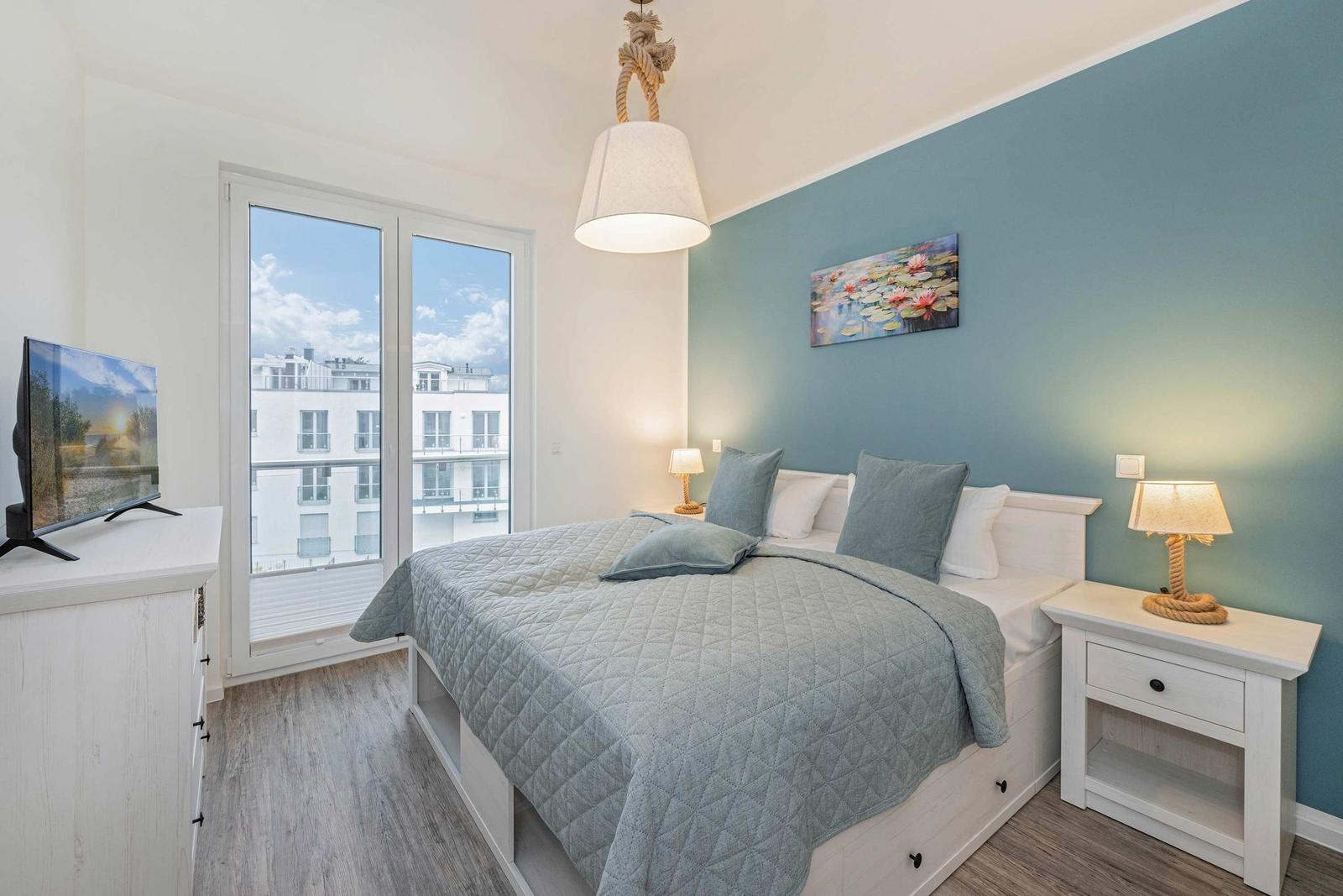 Schlafzimmer mit Bett, Nachttisch, Fernseher und Fenster mit Blick.
