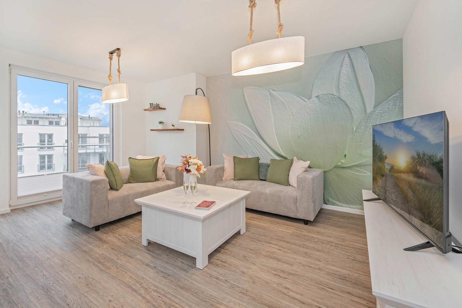 Wohnzimmer mit Sofa, Couchtisch und Fernseher. Wandbild mit Lotusmotiv. Fenster mit Blick auf Gebäude.